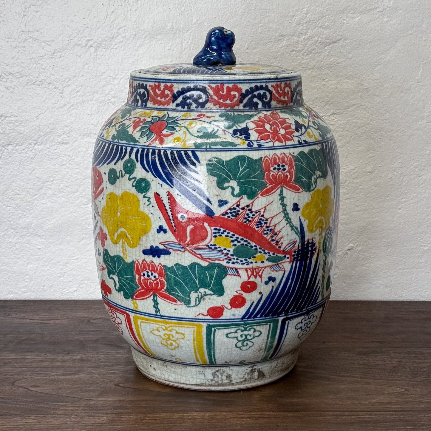 Teal ceramic stool with floral design on a wooden floor against a white wall