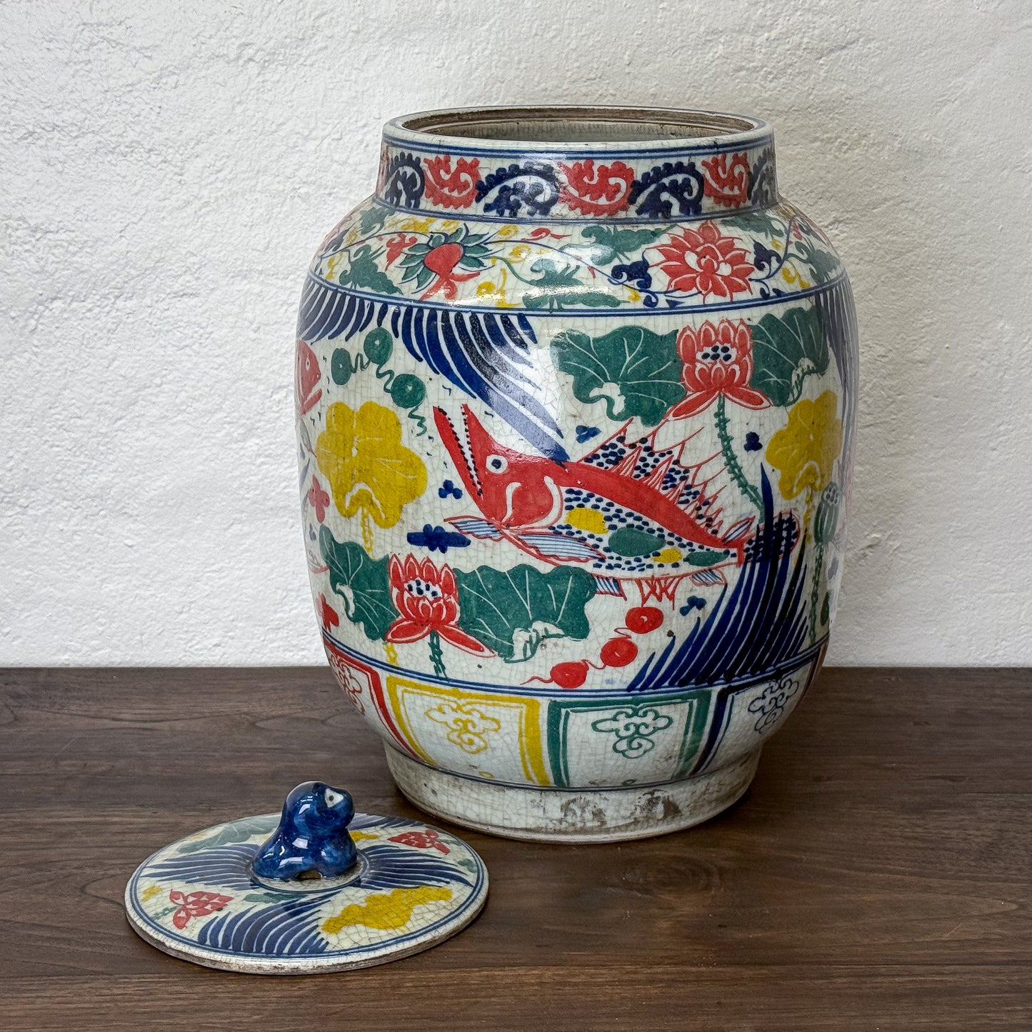 Decorative ceramic jar with colorful floral and fish patterns on a wooden surface.