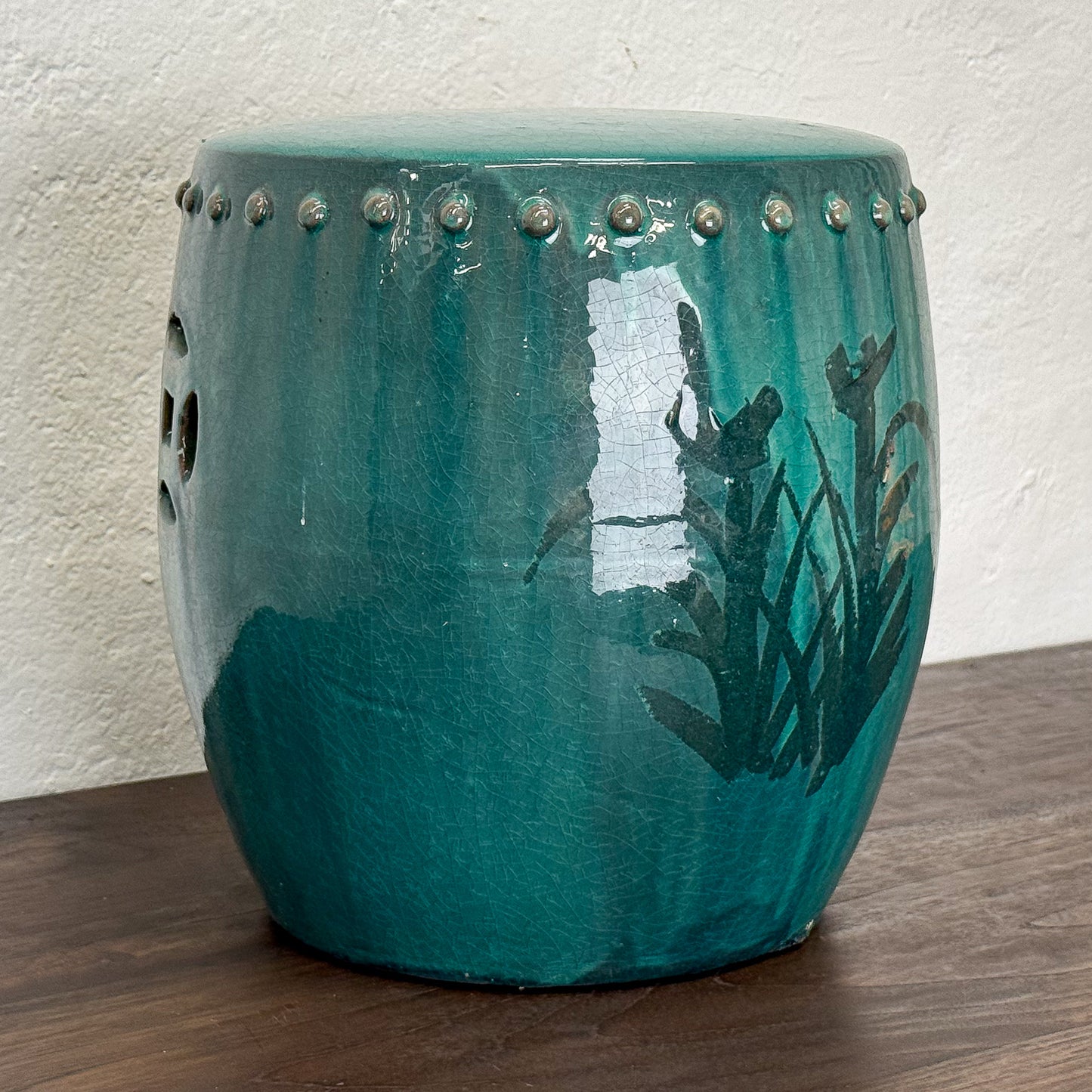 Teal ceramic stool with floral design on a wooden floor against a white wall