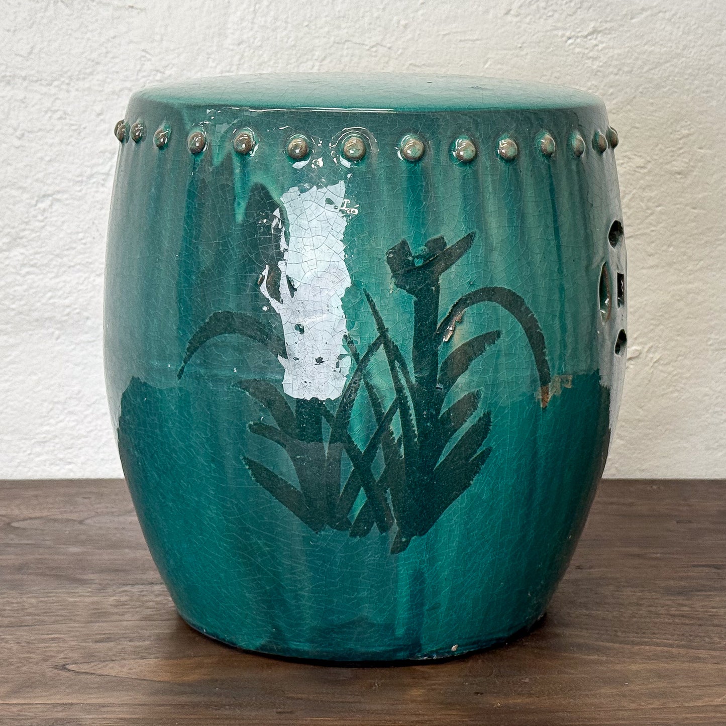 Teal ceramic stool with floral design on a wooden floor against a white wall