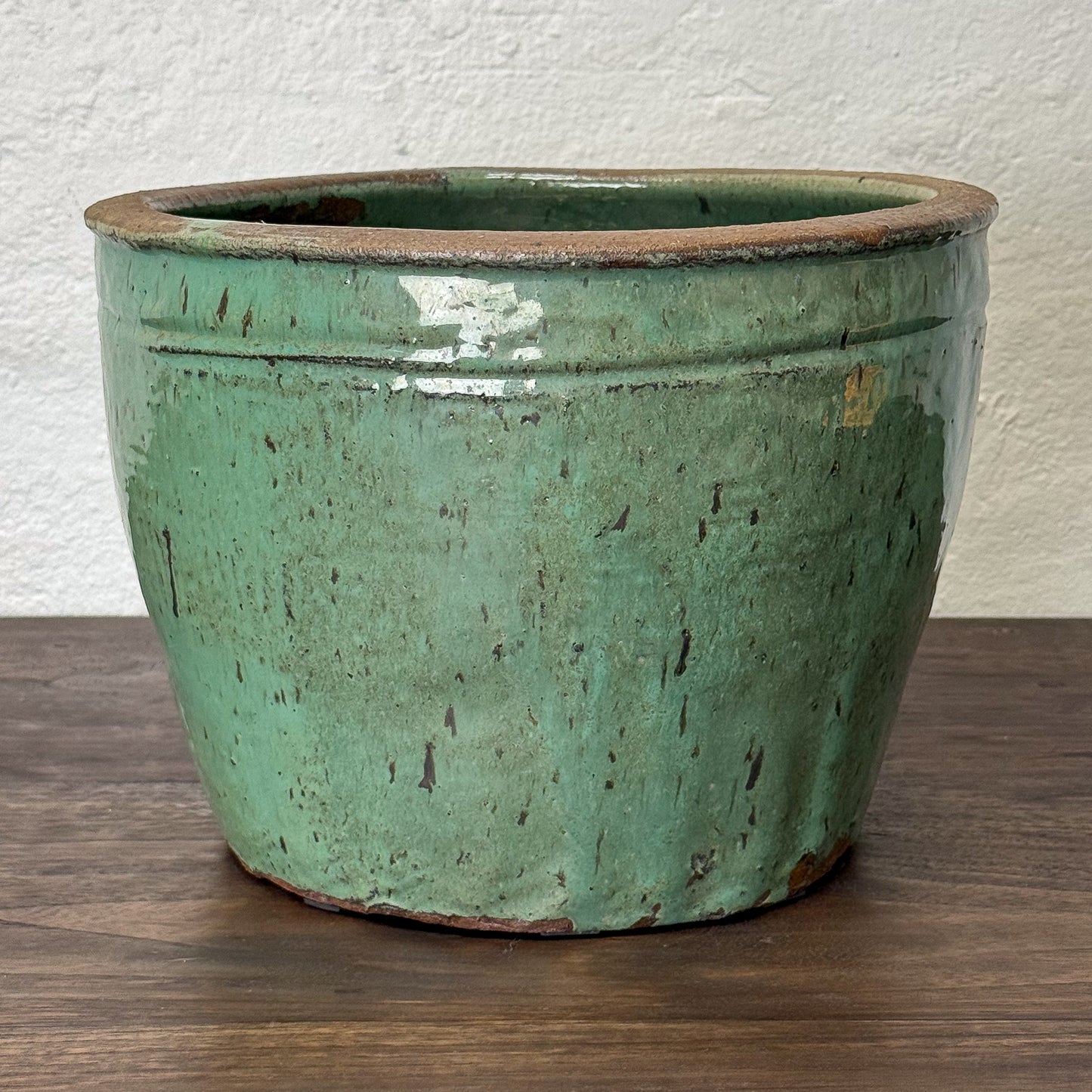 Green ceramic pot on a wooden surface with a white wall background