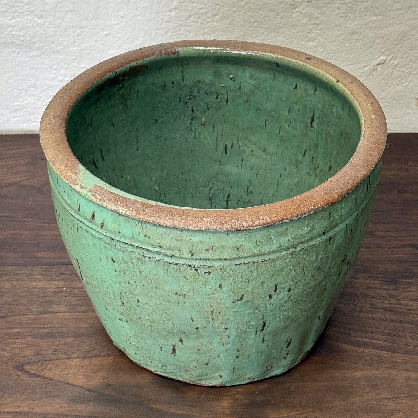 Green ceramic pot on a wooden surface with a white wall background