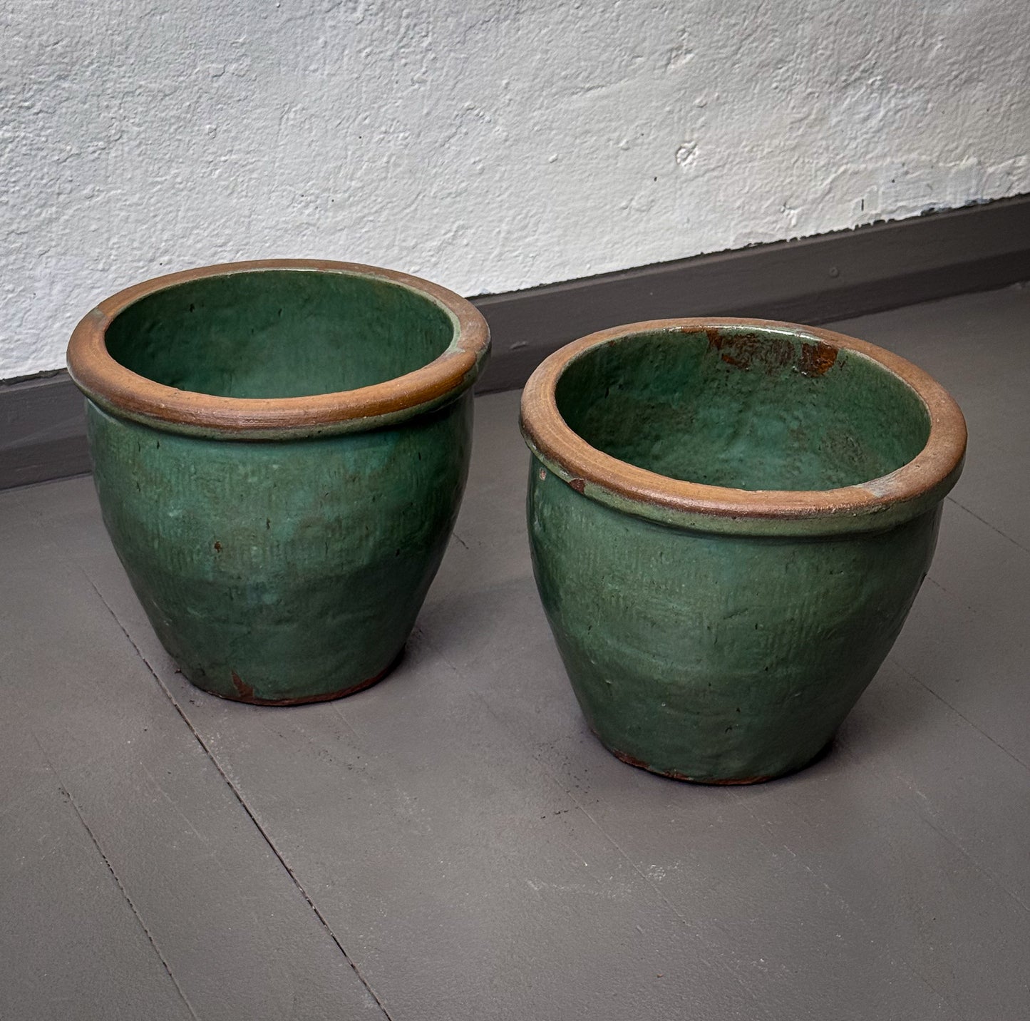 Two green ceramic pots on a gray floor against a white wall.
