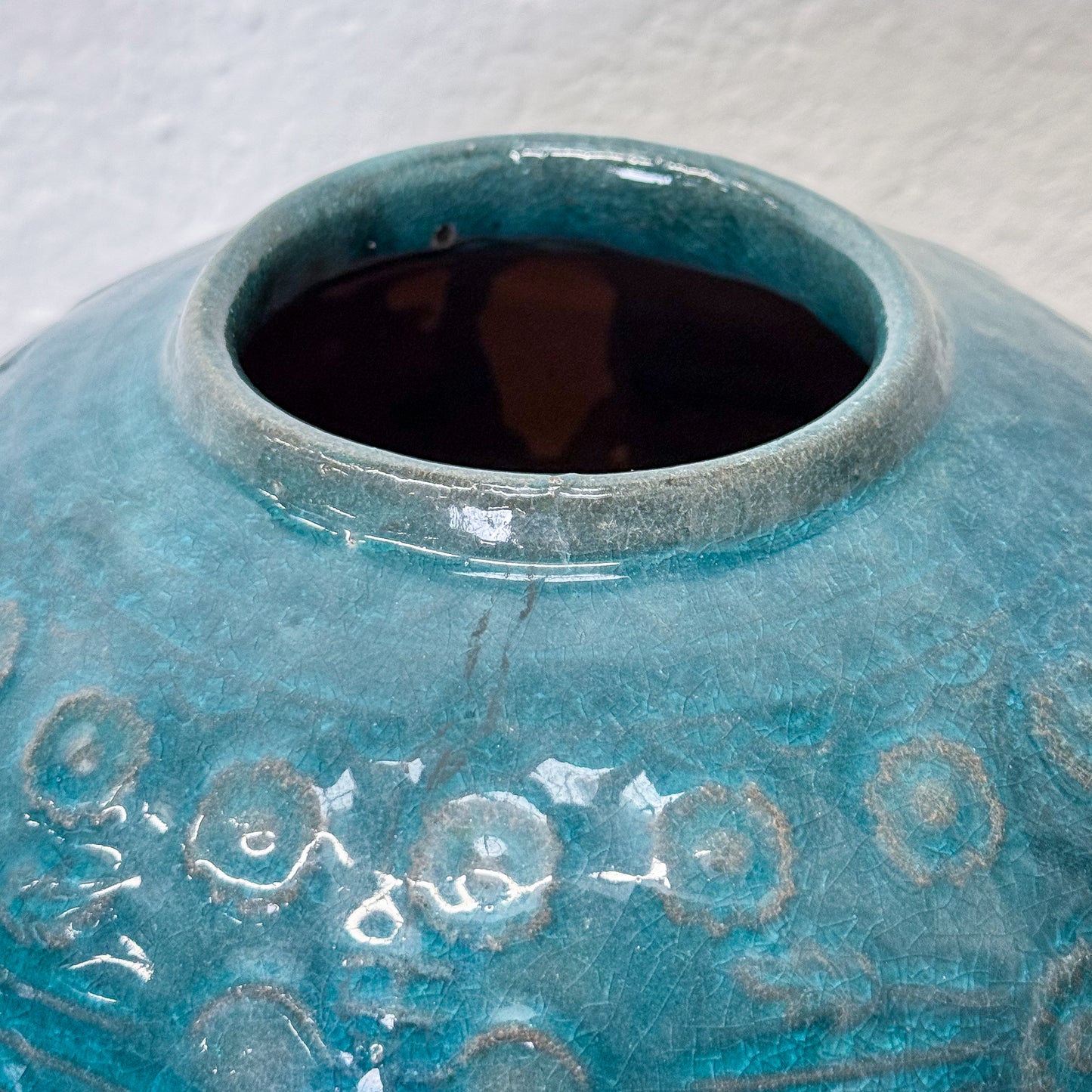 Close-up of a blue ceramic vase with textured surface and floral patterns on a white background