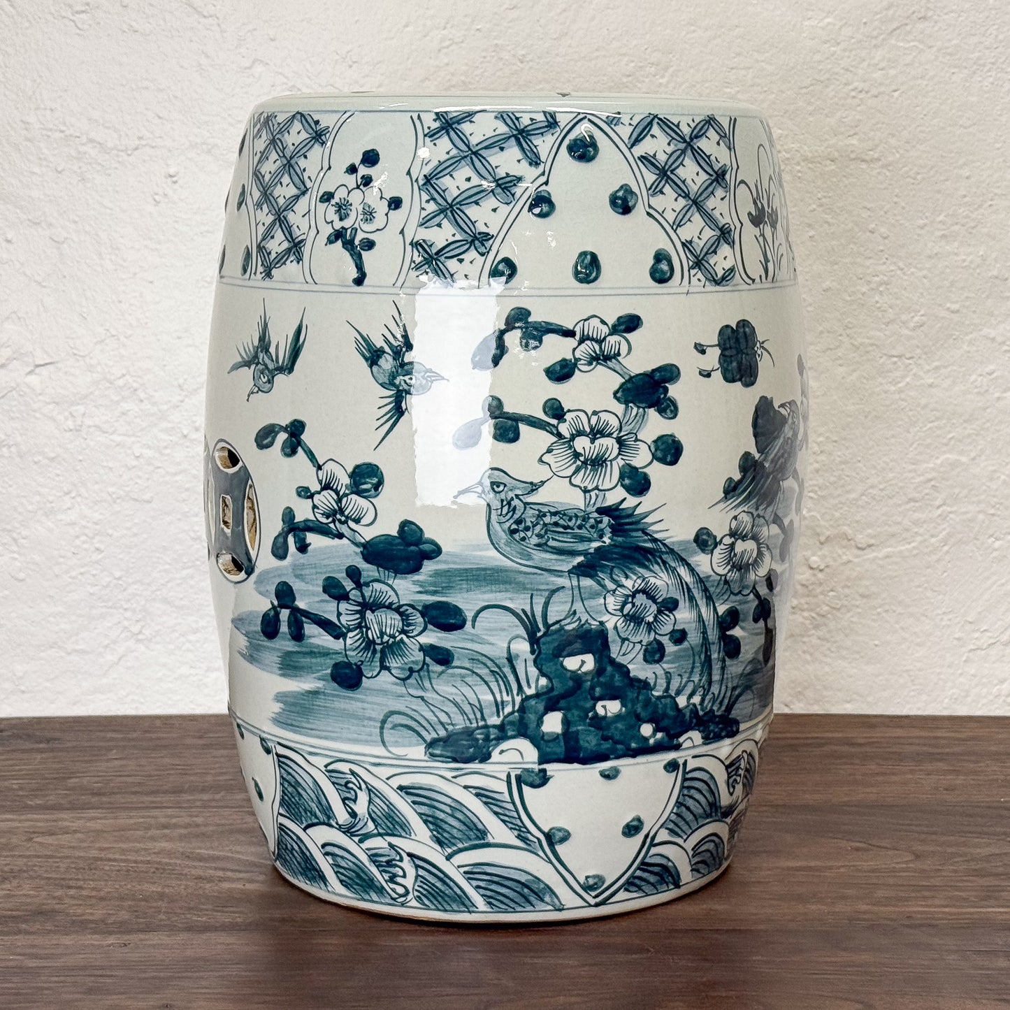 Decorative ceramic stool with blue and white floral and bird pattern on a wooden surface.