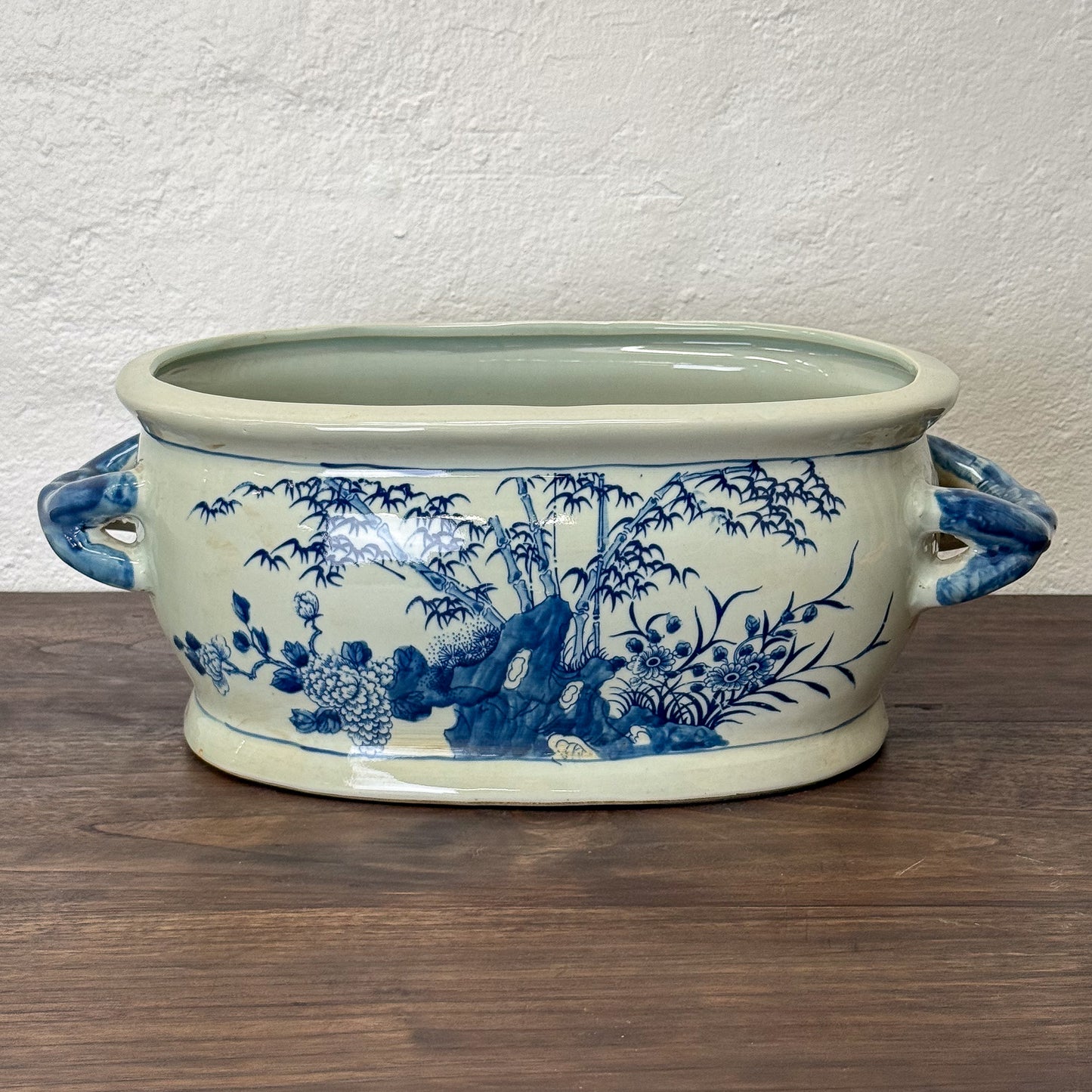 Ceramic planter with blue floral and landscape design on a wooden surface.