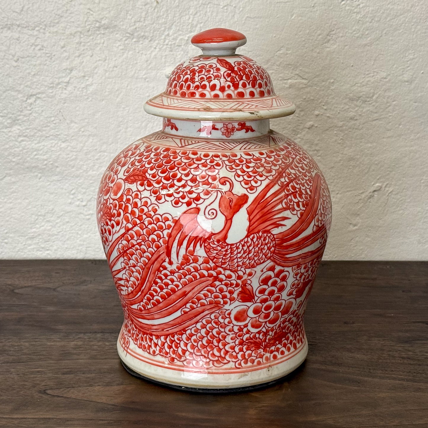 Red and white ceramic jar with phoenix design on a wooden surface.