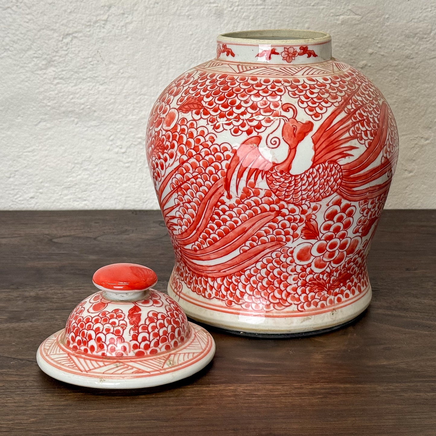 Red and white ceramic jar with phoenix design on a wooden surface.