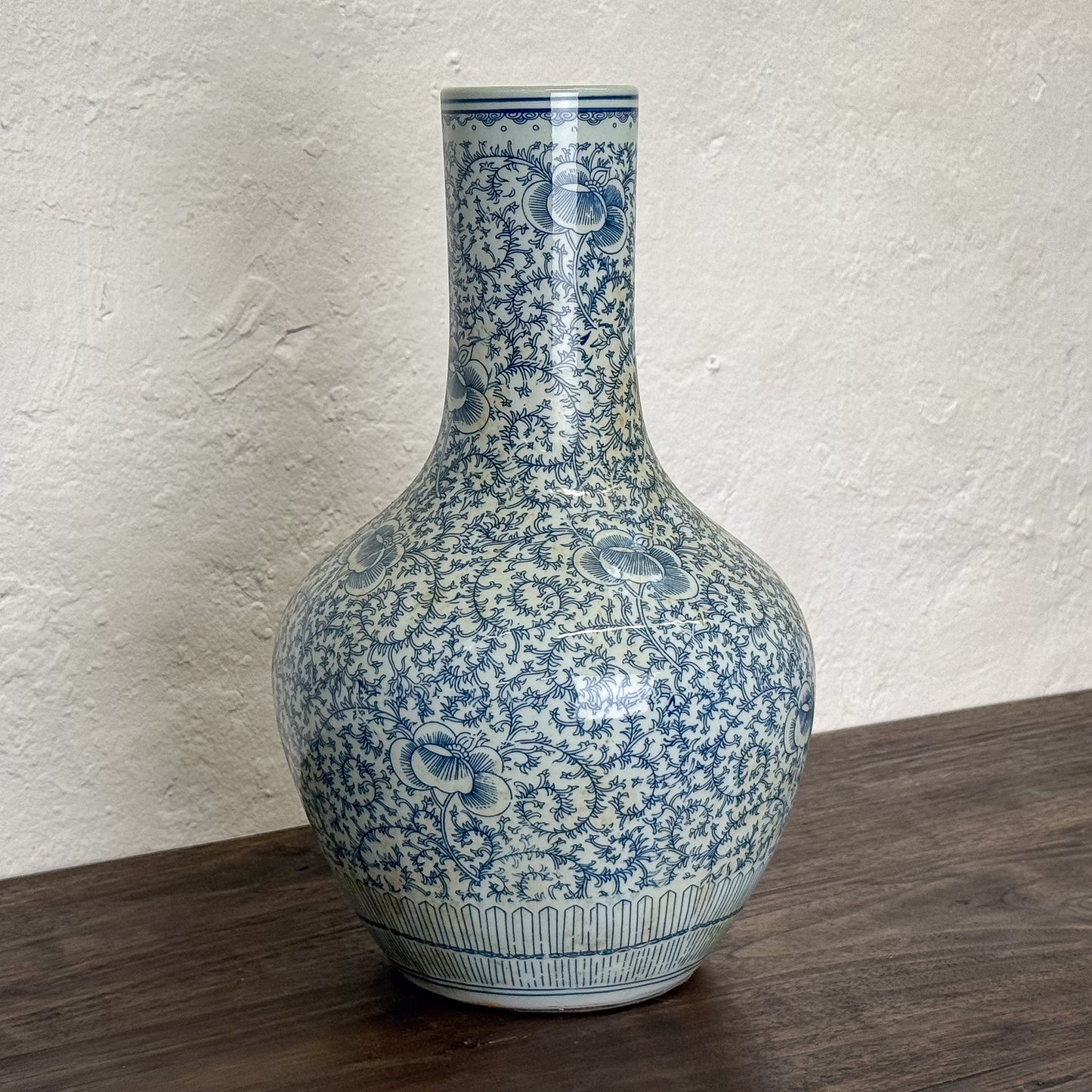 Blue and white floral patterned vase on a wooden surface with a light gray wall background