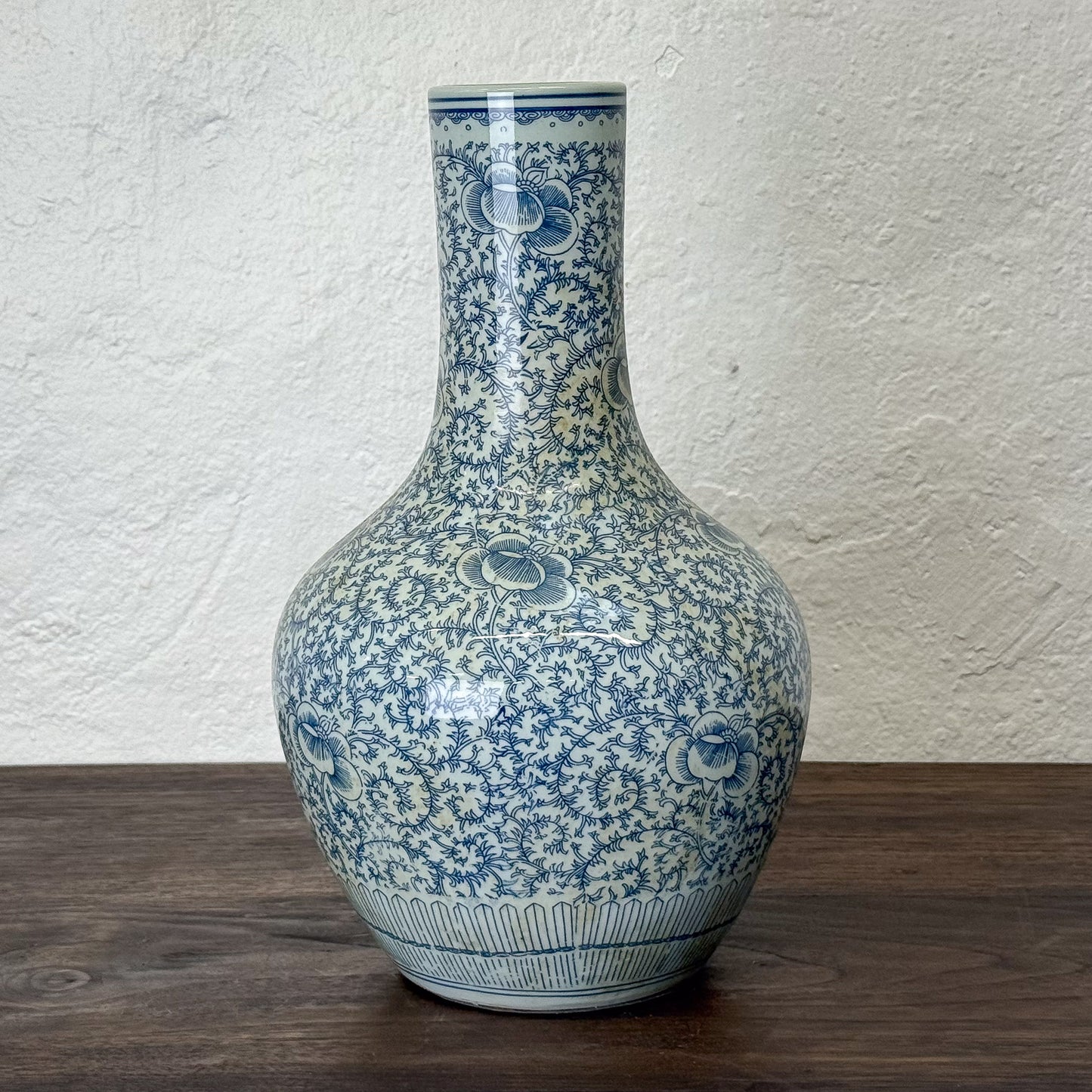 Blue and white floral patterned vase on a wooden surface with a textured white wall background