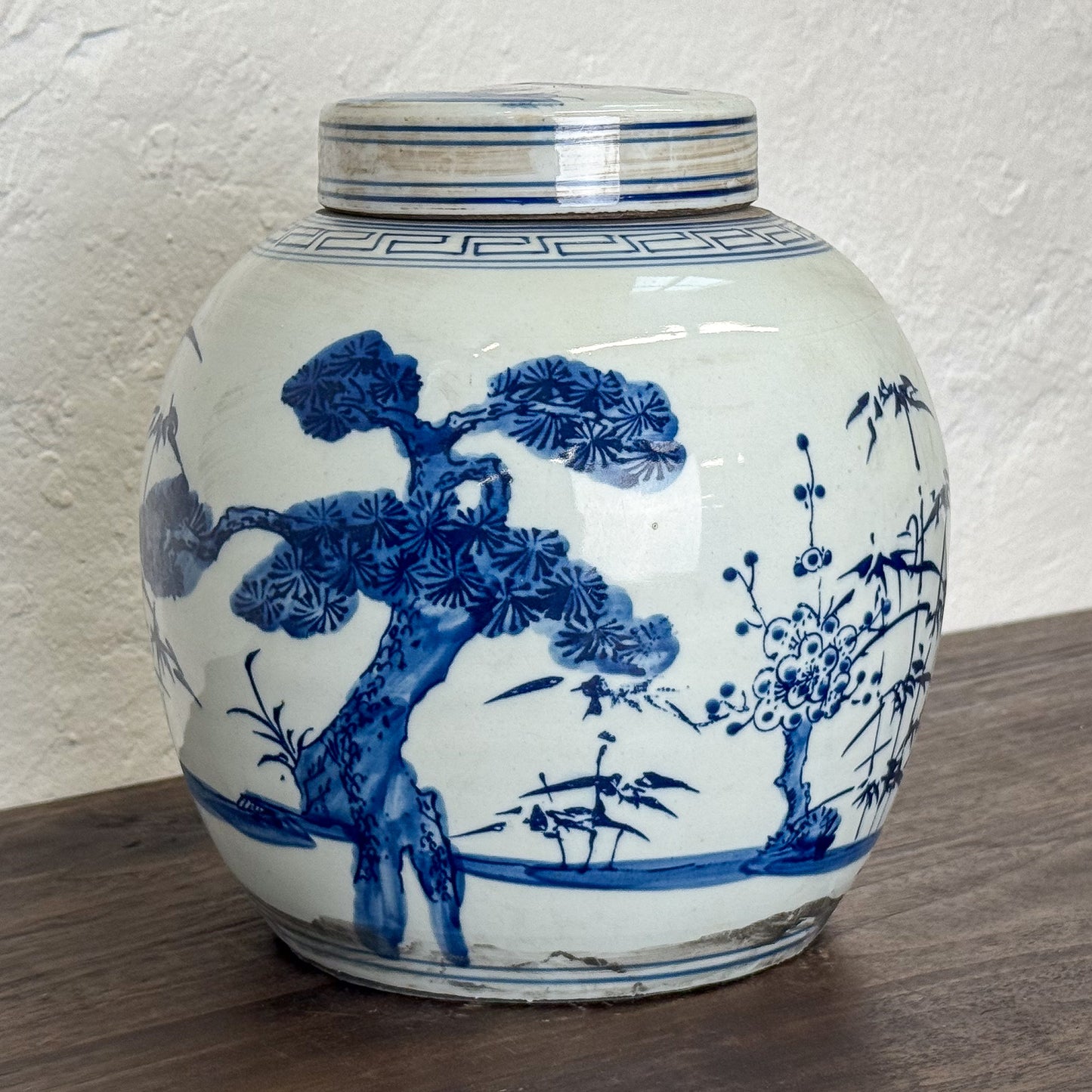 White ceramic jar with blue floral and tree design on a wooden surface.