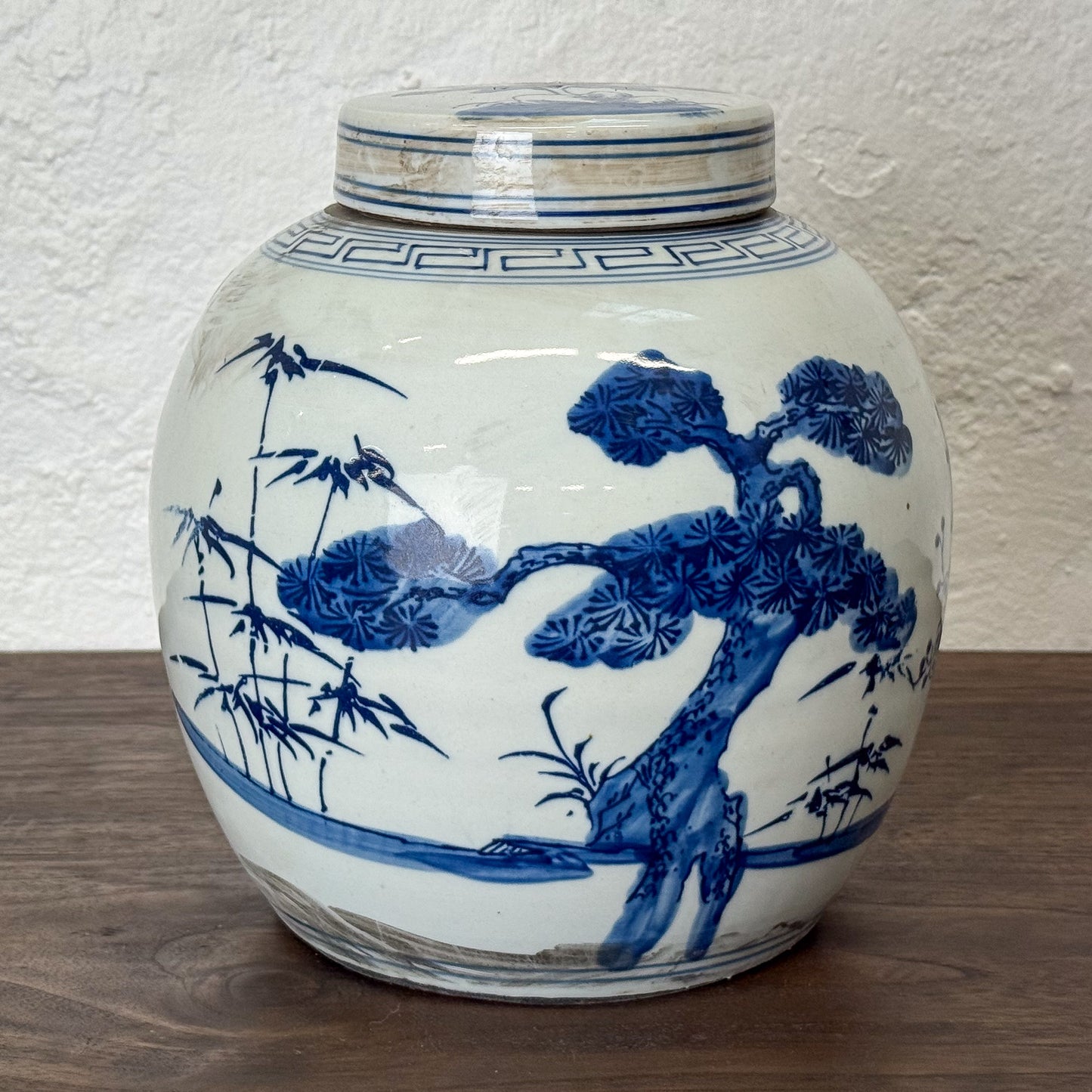 White ceramic jar with blue floral patterns on a wooden surface and white wall background