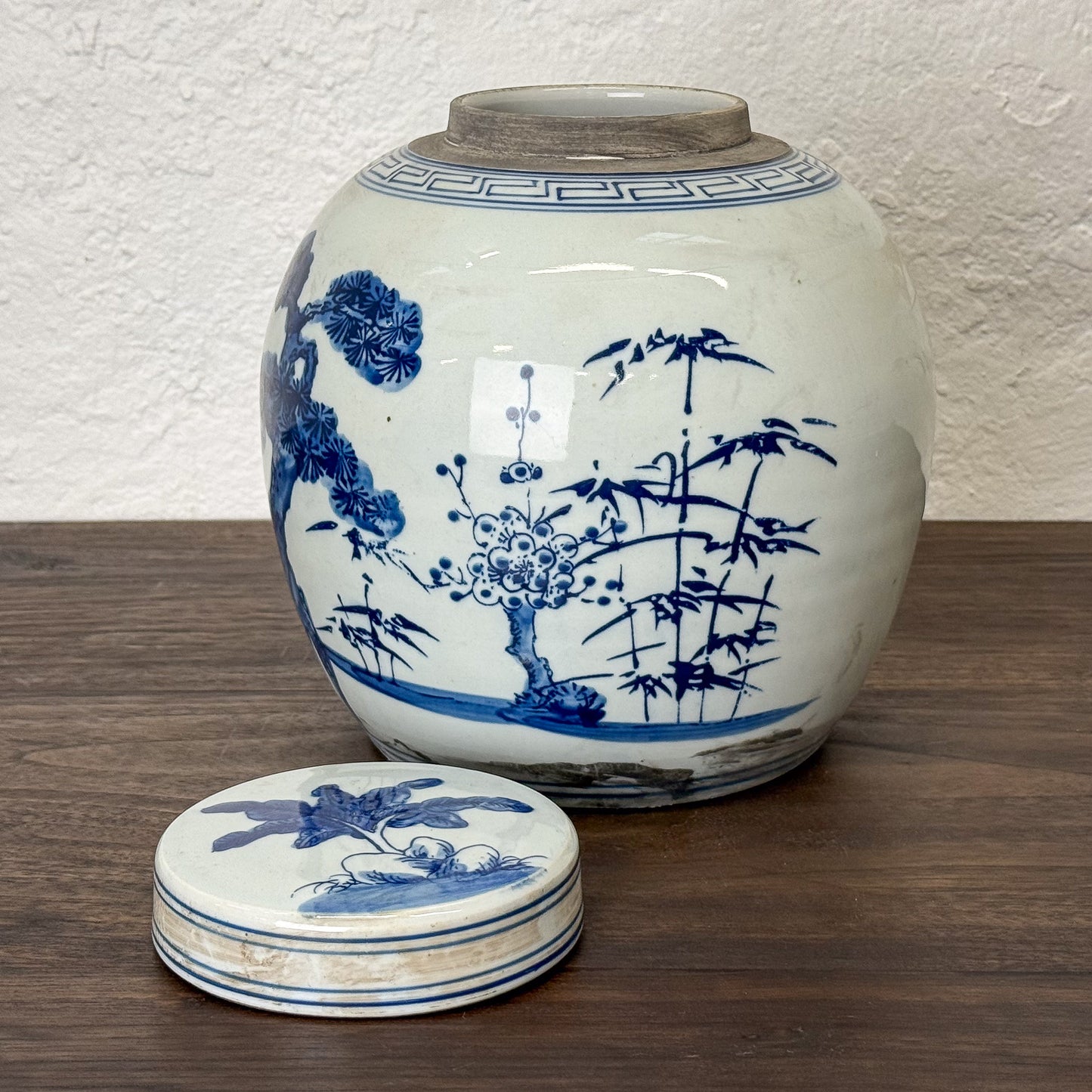 White ceramic jar with blue floral and landscape design on a wooden surface.