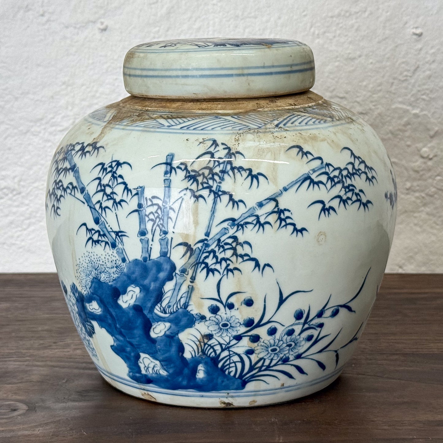 Blue and white ceramic jar with floral and bamboo design on a wooden surface.