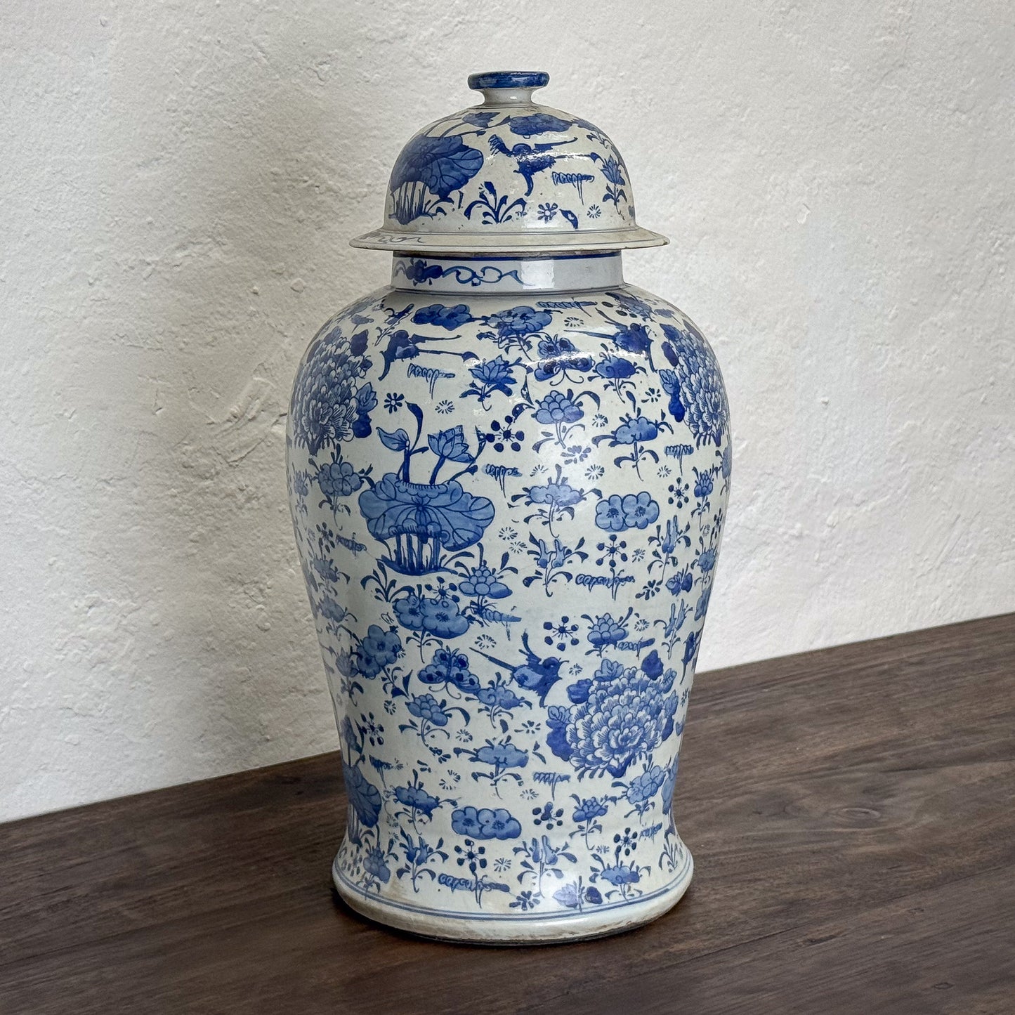 Blue and white floral-patterned ceramic jar with lid on a wooden surface against a textured white wall.