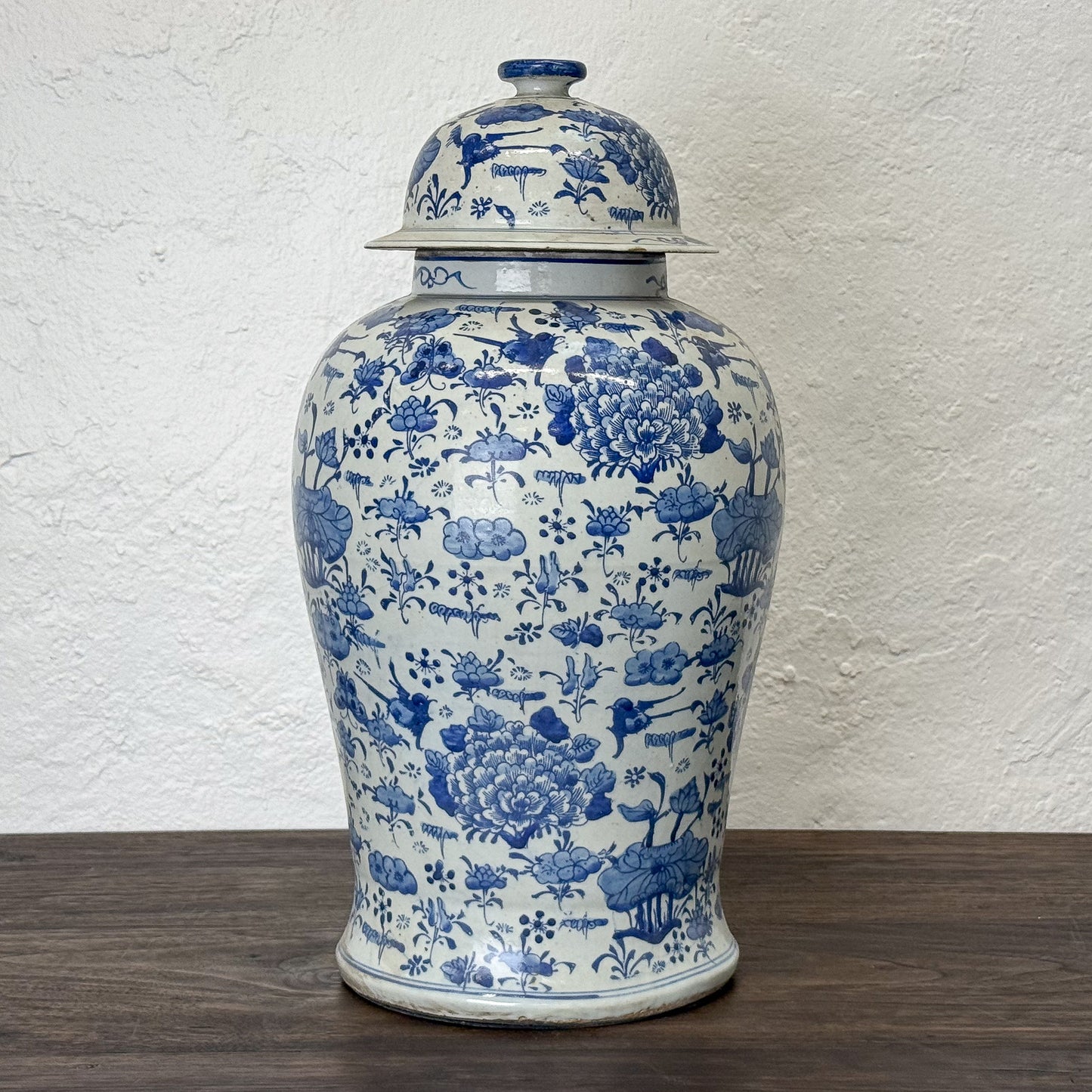 Blue and white ceramic jar with floral patterns on a wooden surface and white textured wall background