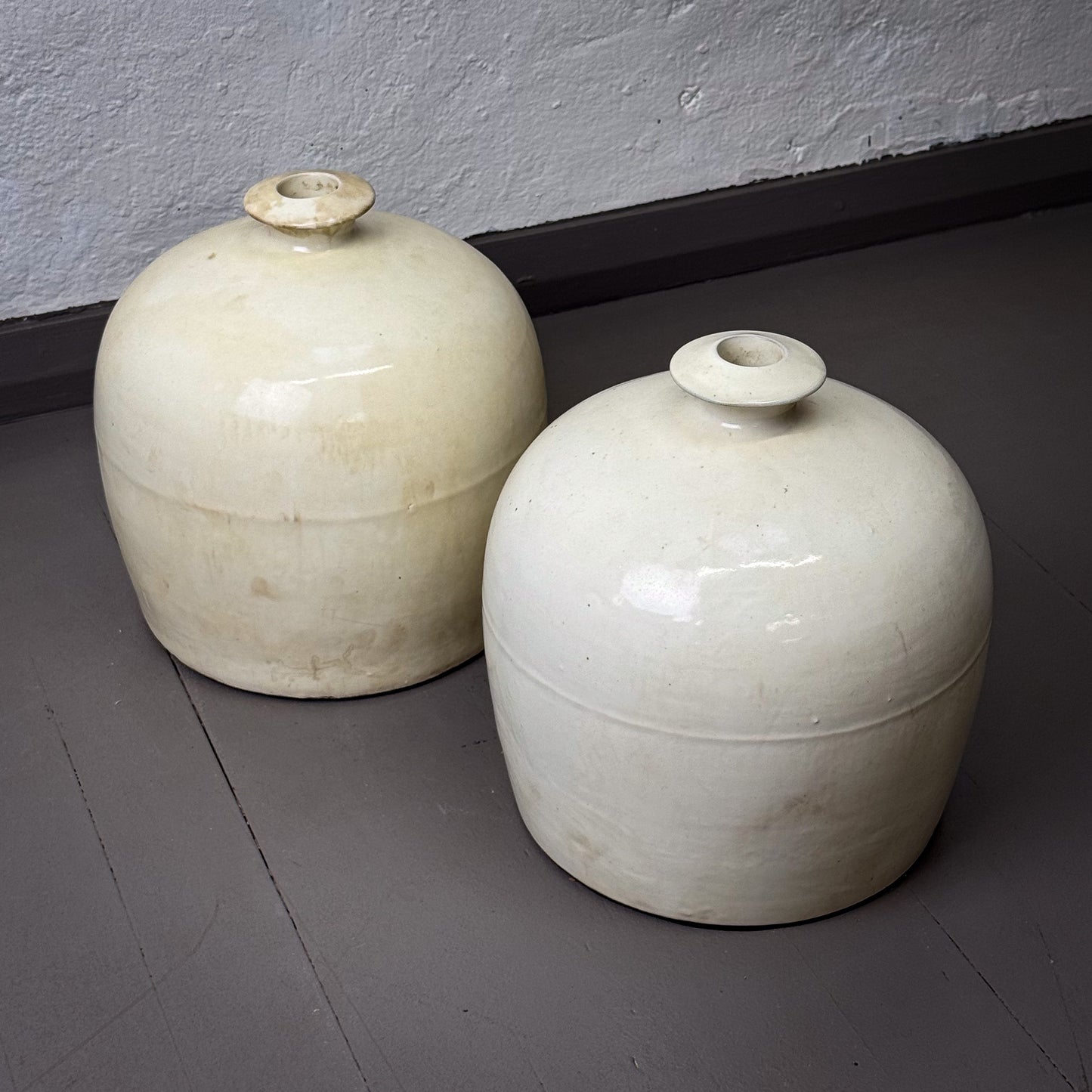 Two white ceramic jars on a gray floor against a plain wall.
