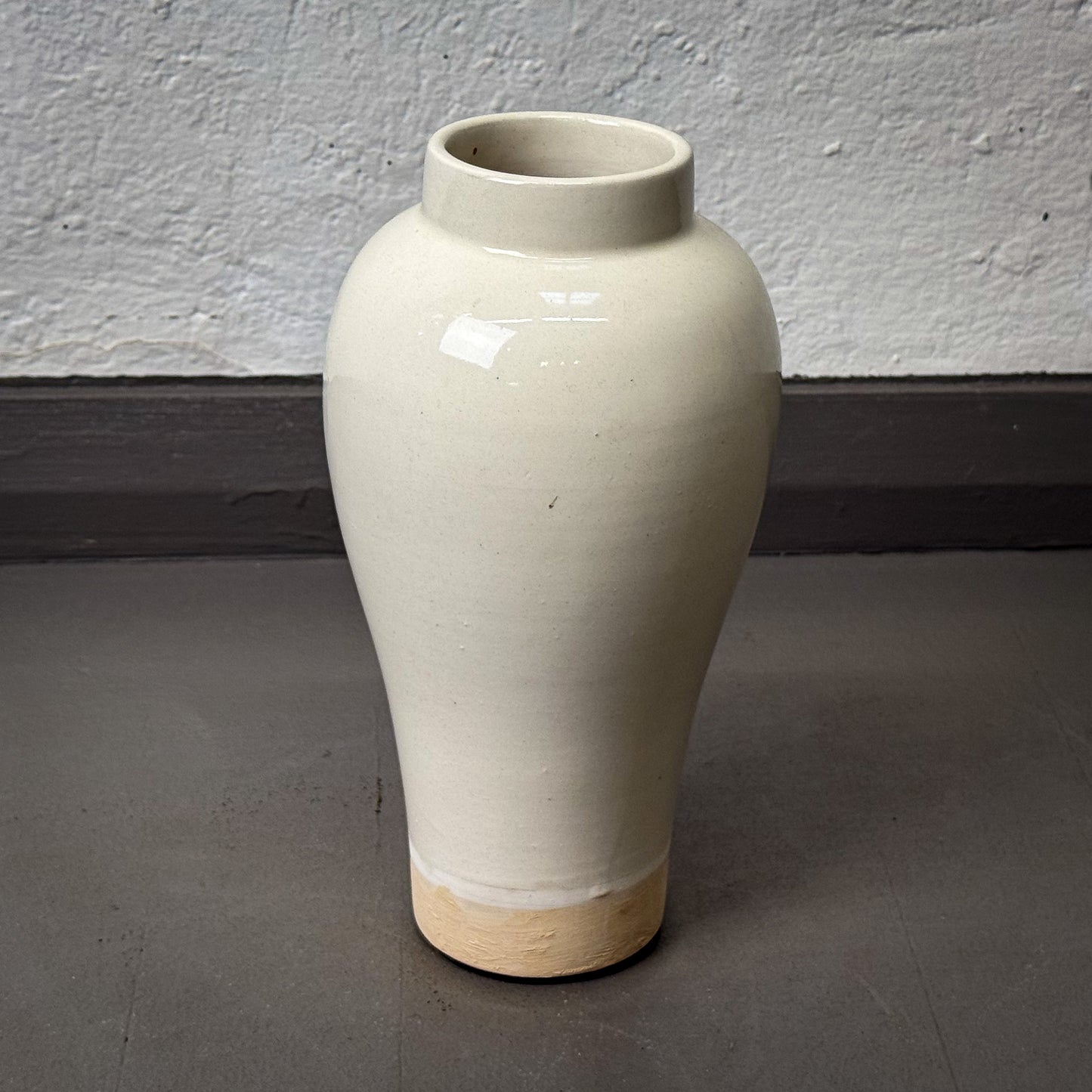 White ceramic vase on a gray floor with a white wall background