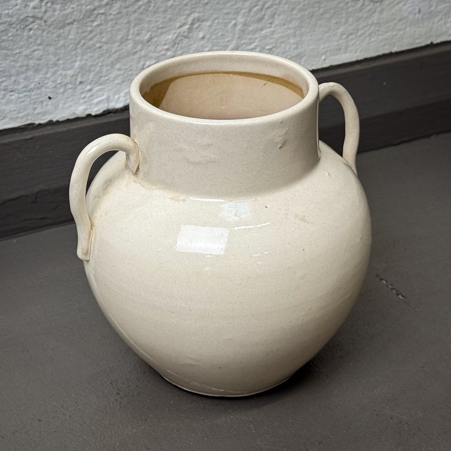 White ceramic vase with handles on a gray surface.
