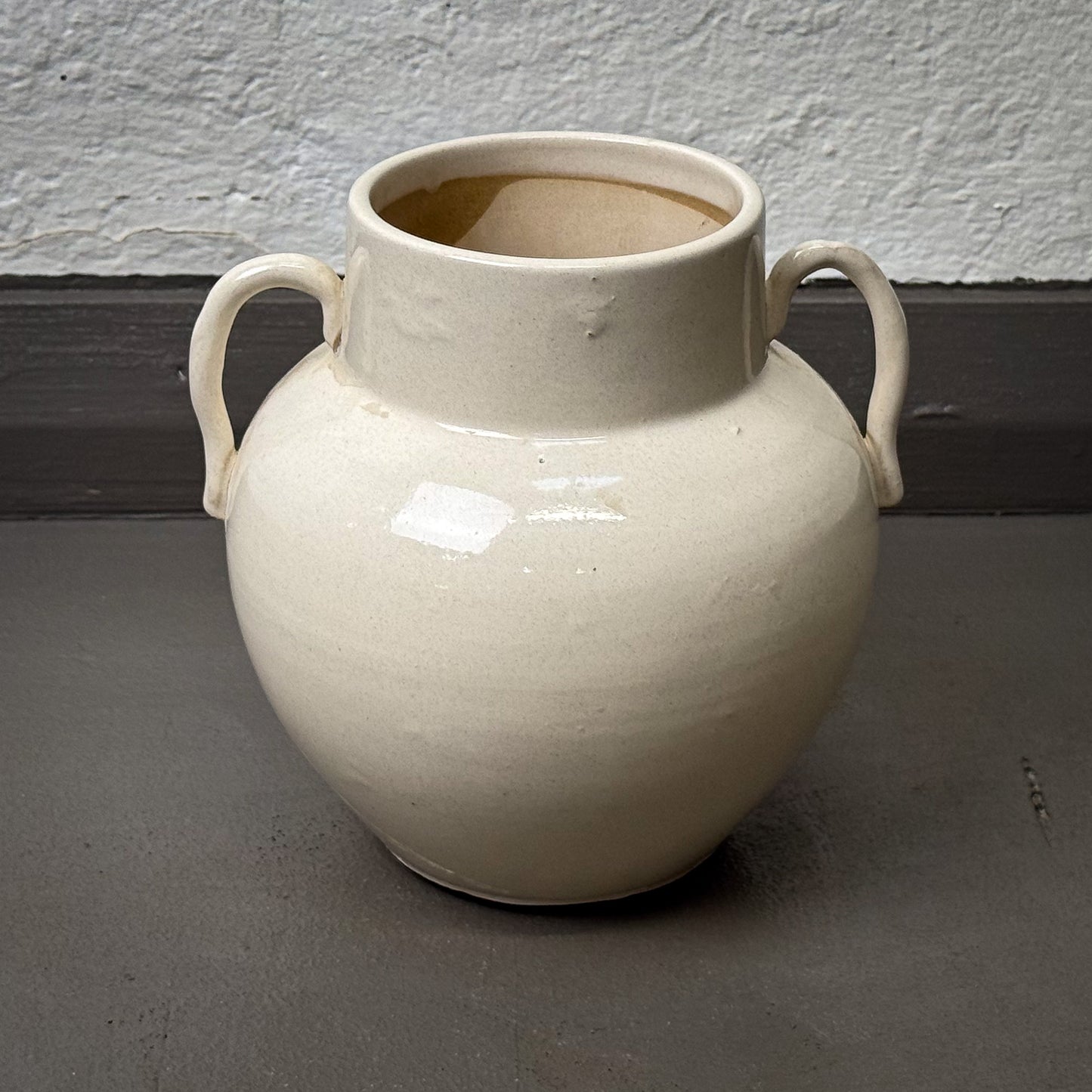 White ceramic vase with handles on a gray surface against a white wall.