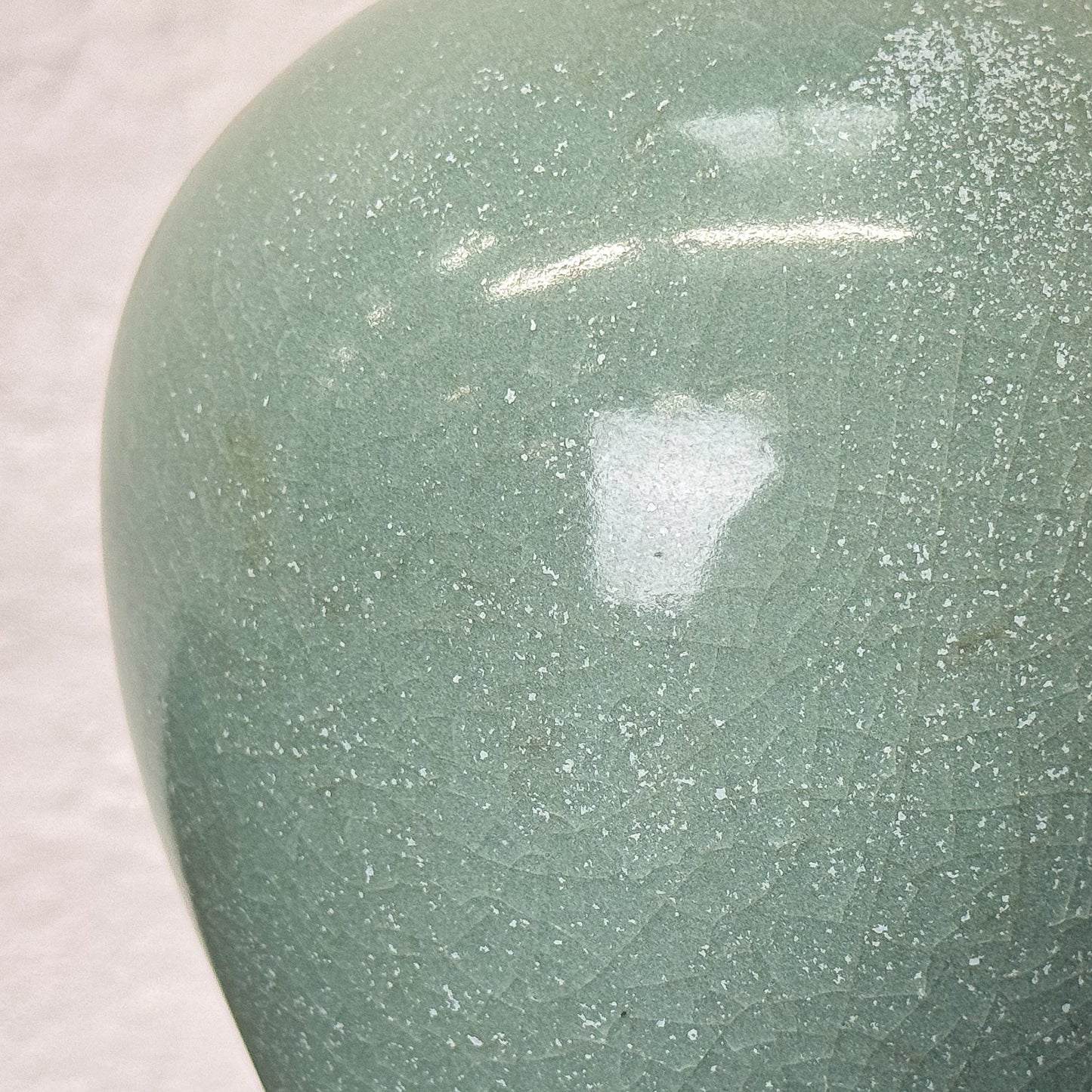 Close-up of a green ceramic vase with speckled texture on a light background