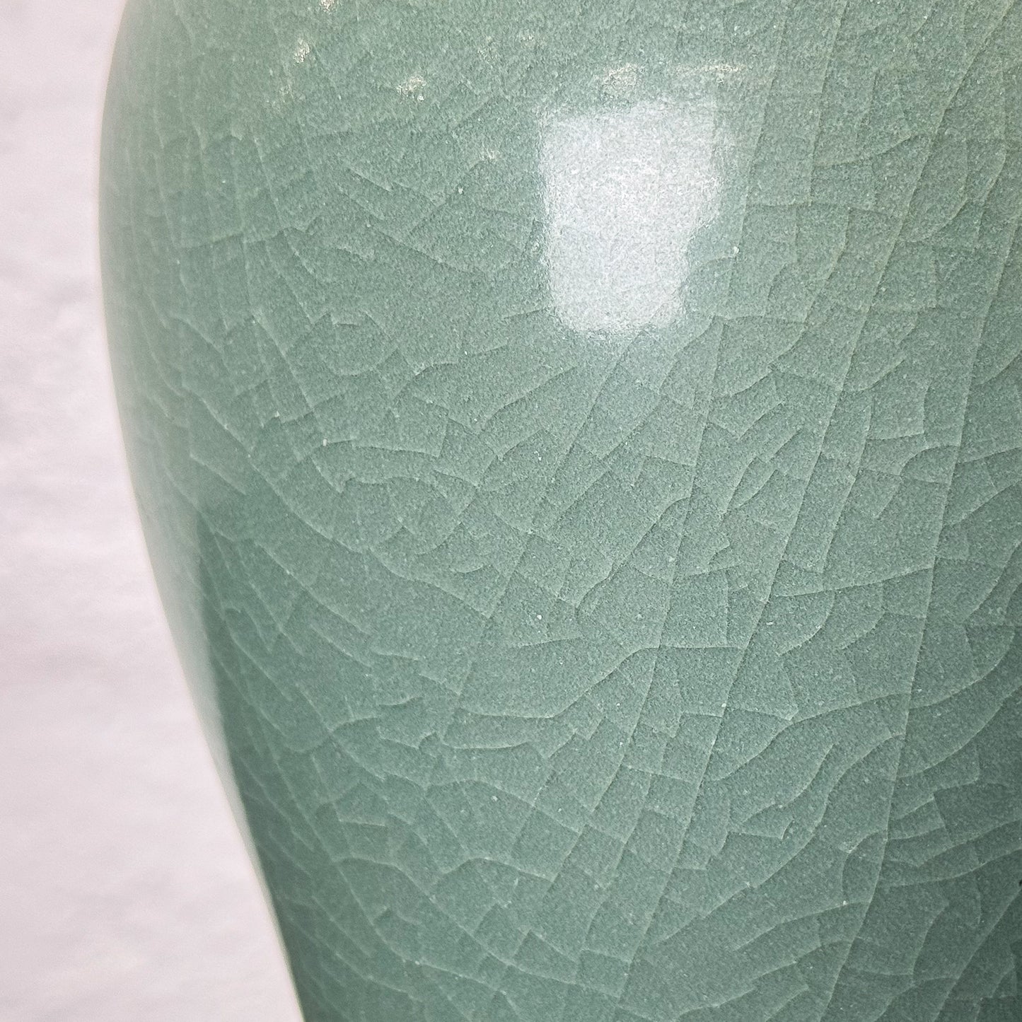 Green ceramic vase on a wooden surface with a textured white wall background