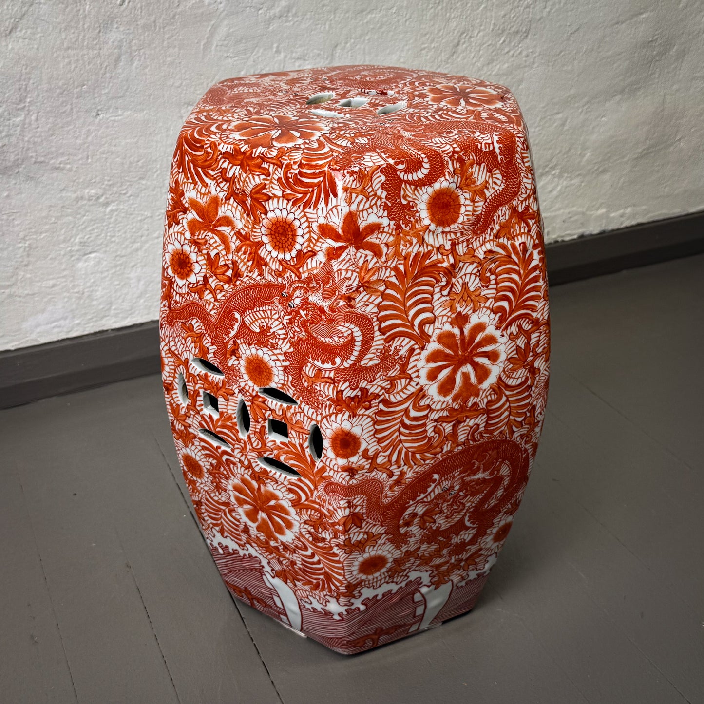 Decorative ceramic stool with intricate red and white patterns on a plain floor.