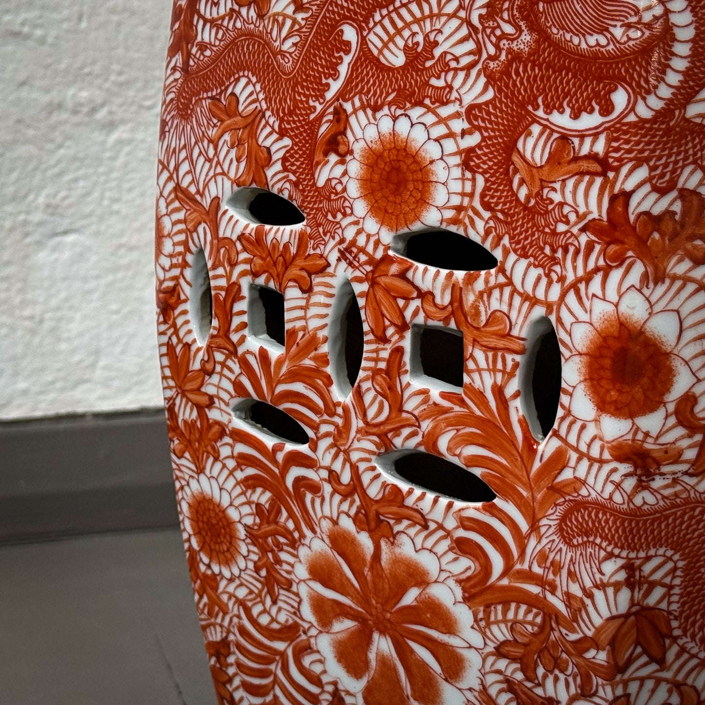 Ceramic stool with red floral and dragon design on a textured white background