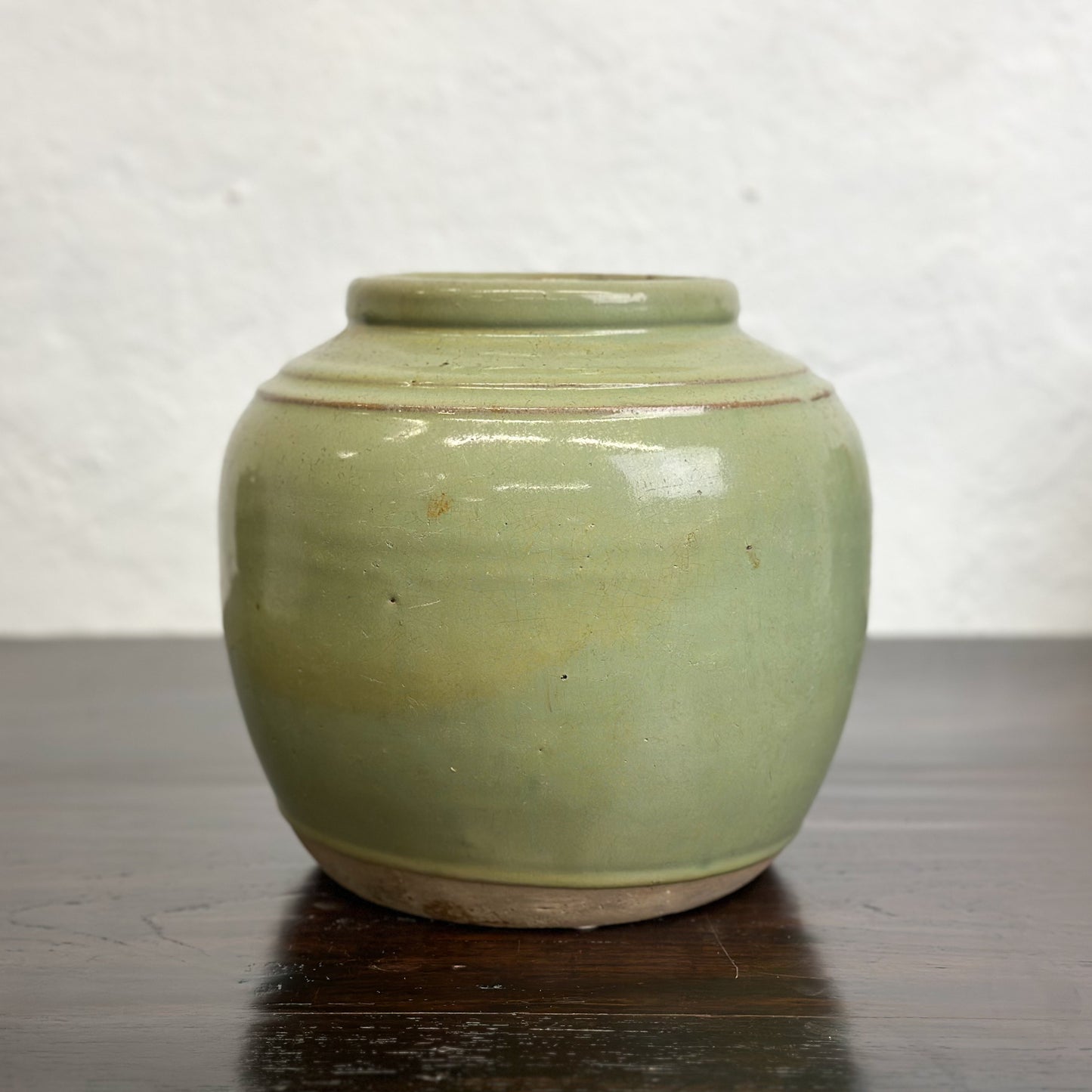 A squat Chinese stoneware pot with a celadon green glaze and a double ridge shoulder.