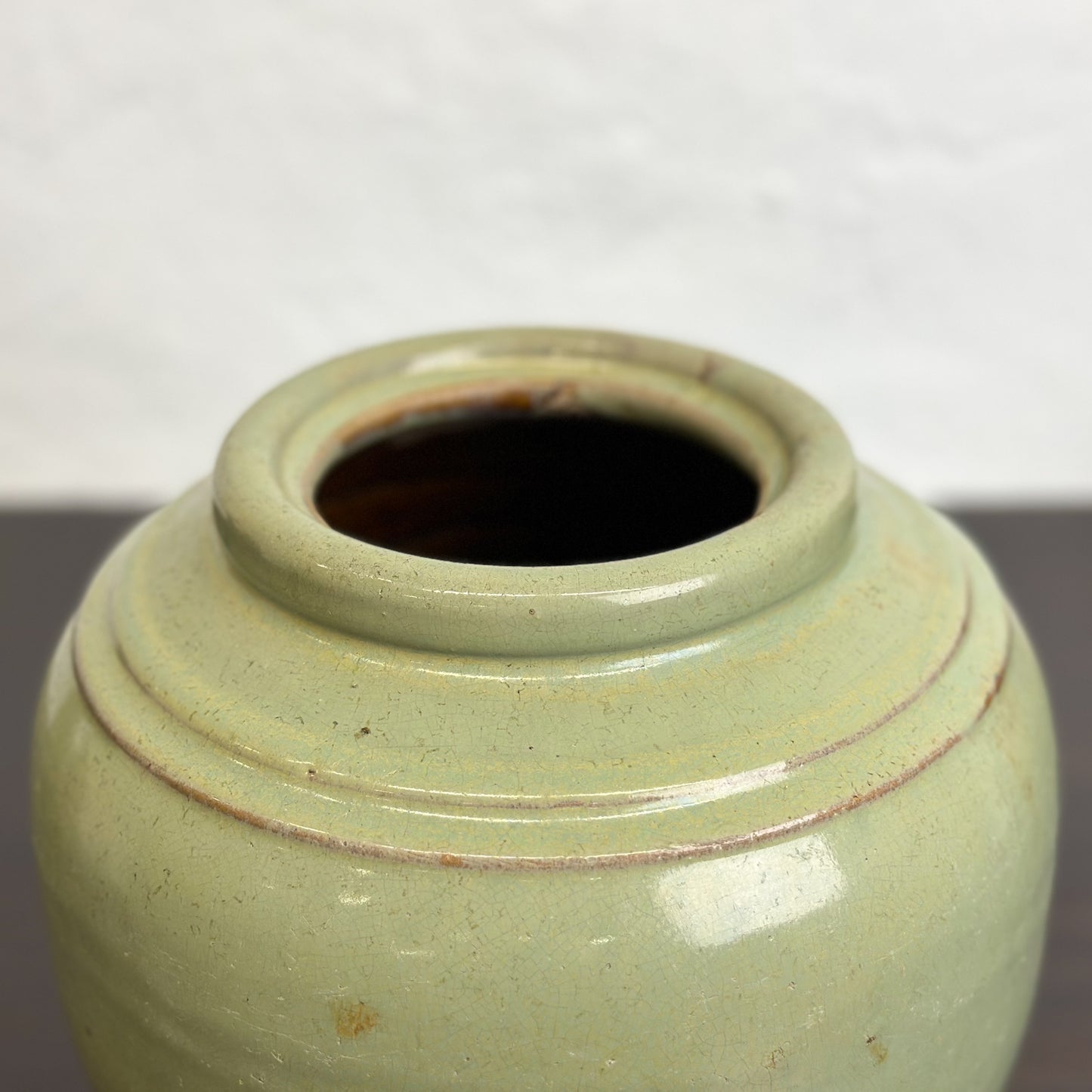 A squat Chinese stoneware pot with a celadon green glaze and a double ridge shoulder.