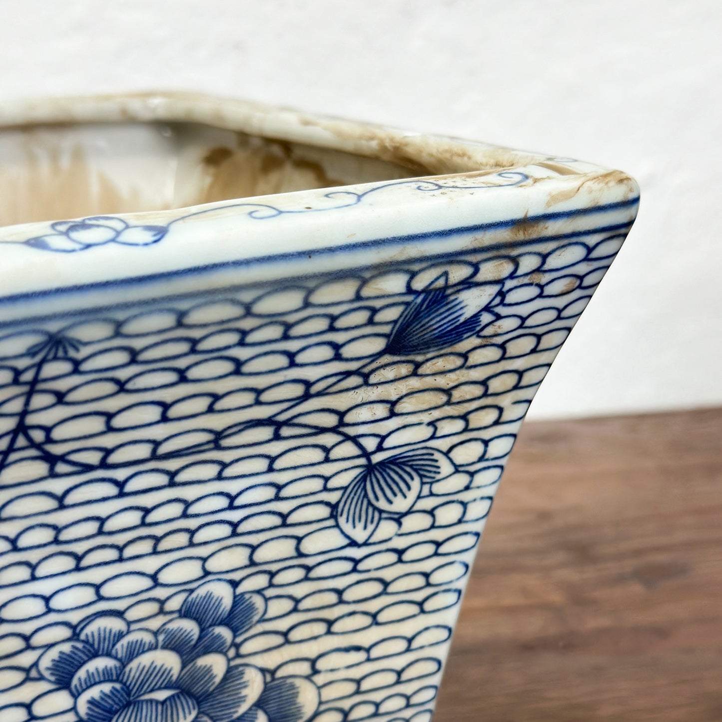 Two square porcelain planters with a blue floral pattern on a beige background, displayed on a wooden surface against a plain wall.