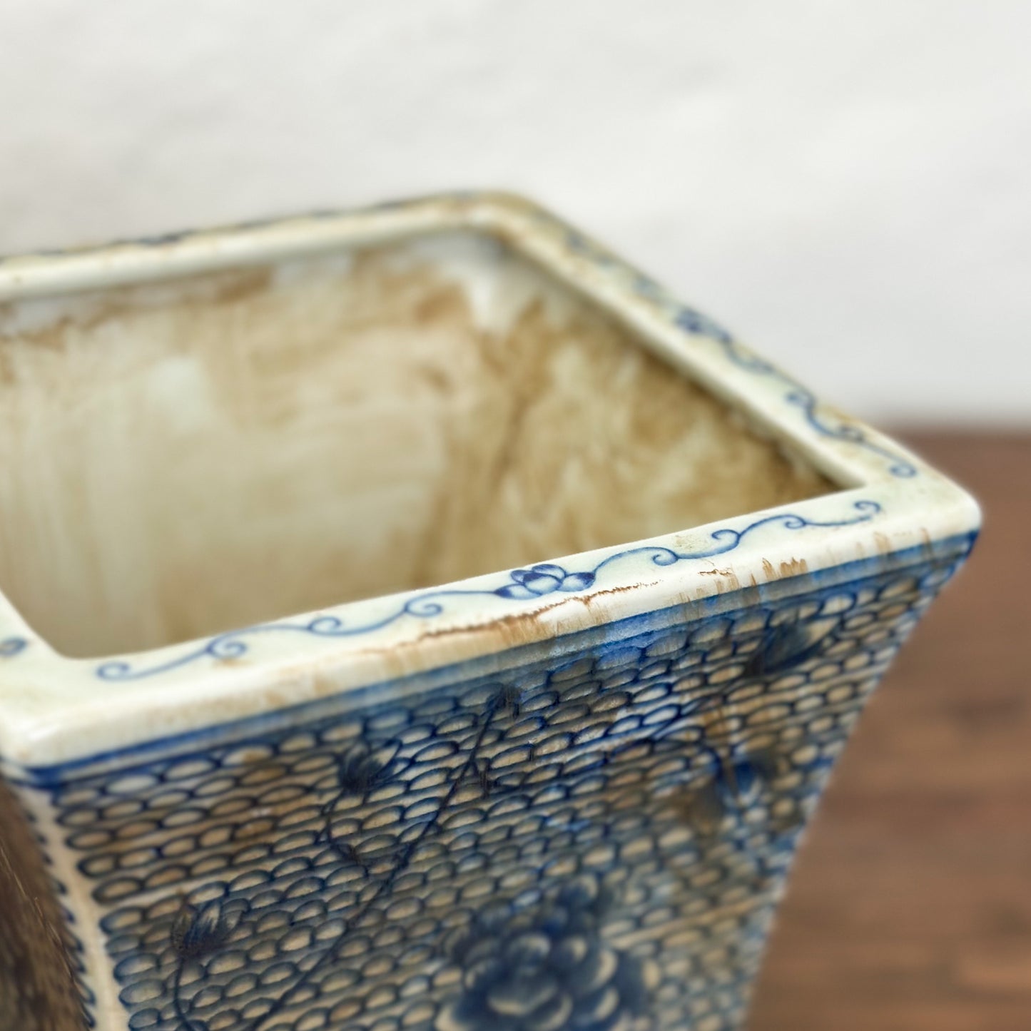 Two square porcelain planters with a blue floral pattern on a beige background, displayed on a wooden surface against a plain wall.