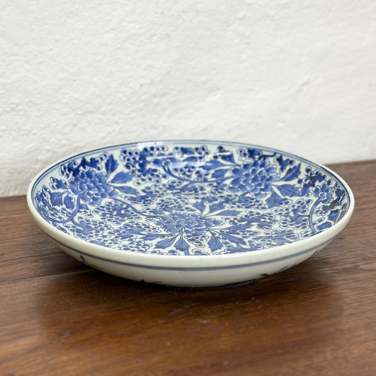 A round porcelain plate with blue floral patterns on a white background, displayed on a wooden surface.