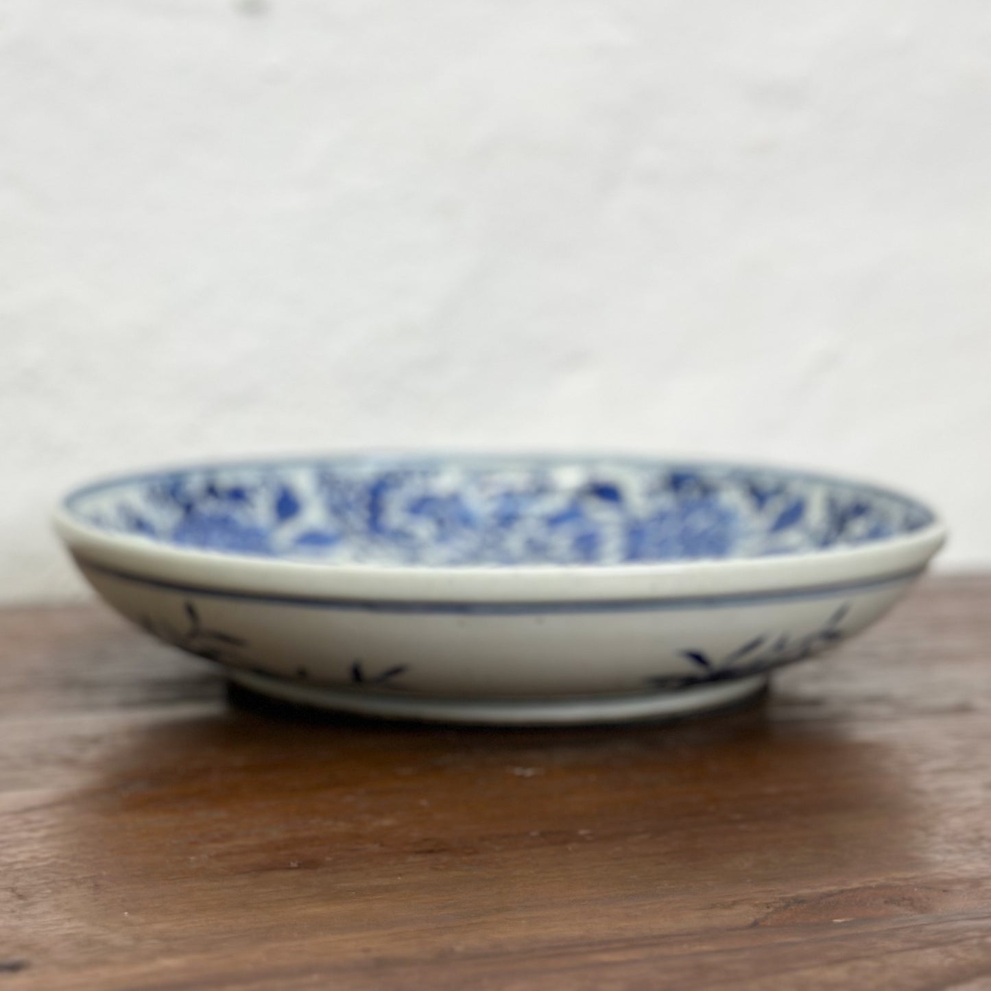 A round porcelain plate with blue floral patterns on a white background, displayed on a wooden surface.