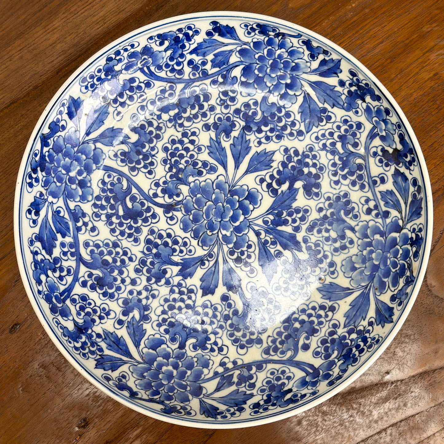 A round porcelain plate with blue floral patterns on a white background, displayed on a wooden surface.