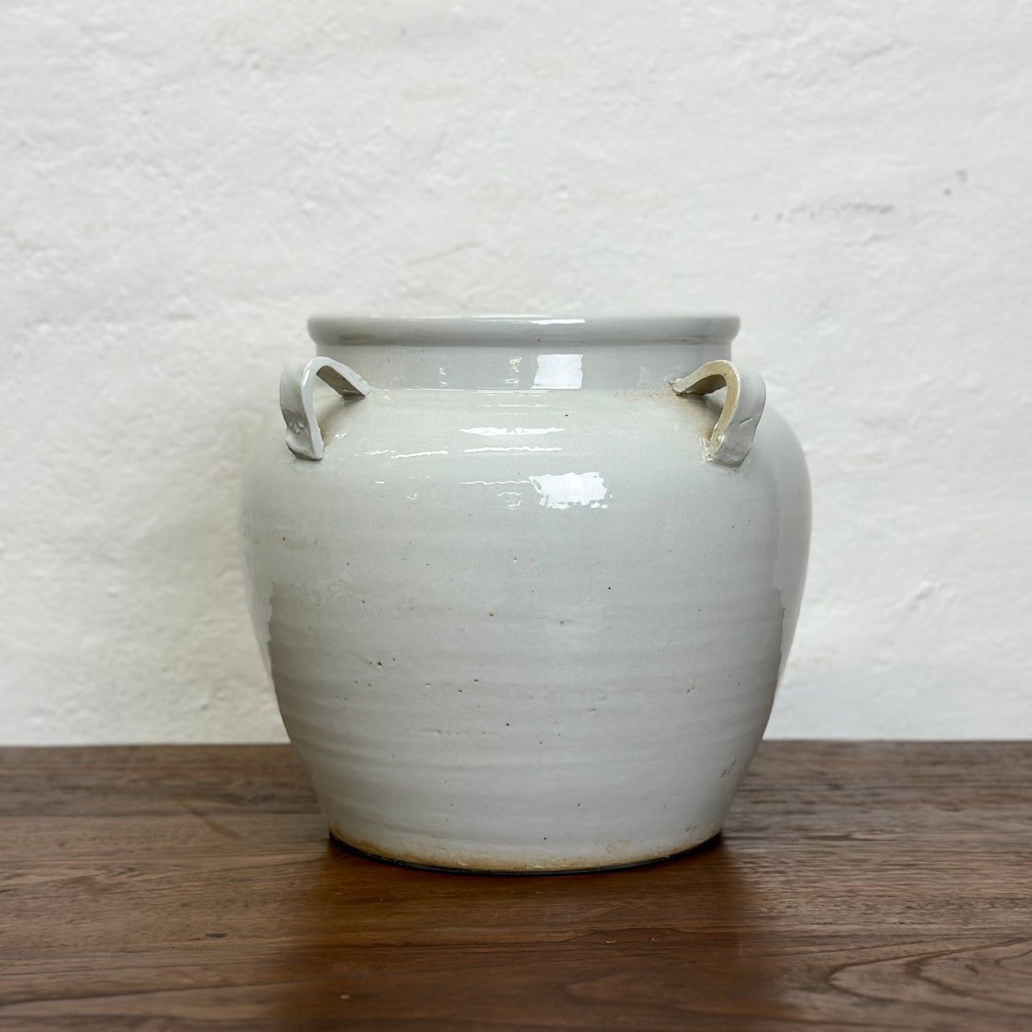 A simple beige porcelain vase with four handles, placed against a plain background on a wooden surface.