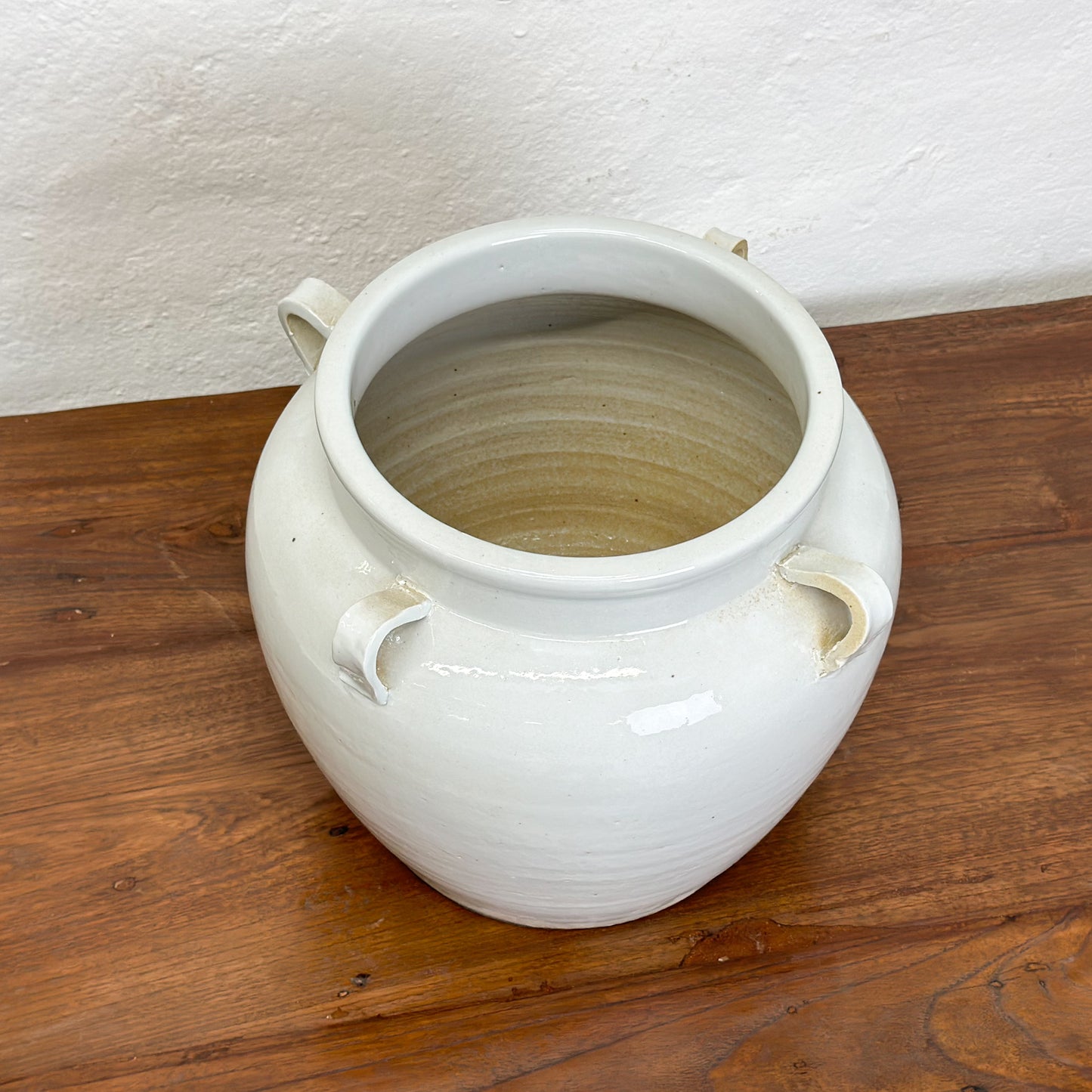 A simple beige porcelain vase with four handles, placed against a plain background on a wooden surface.