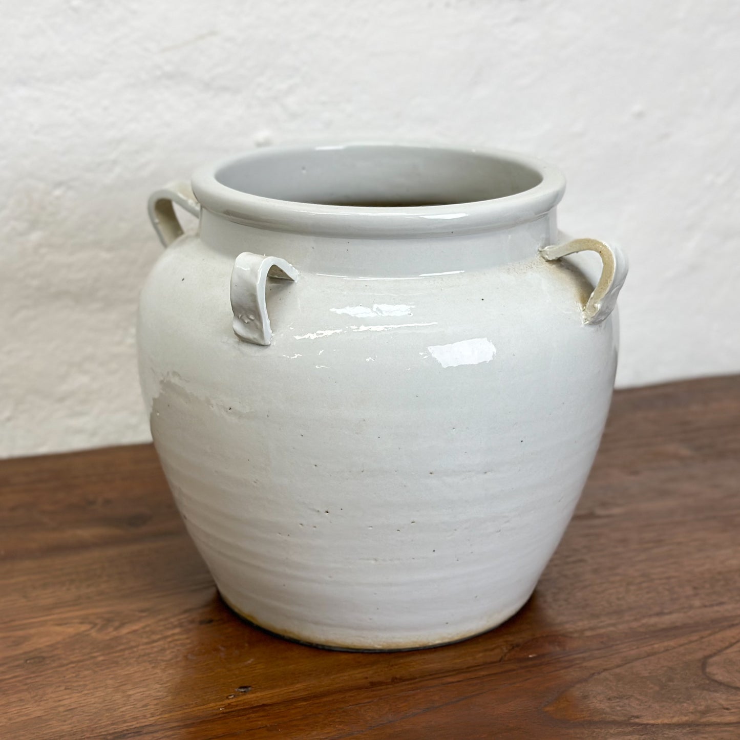 A simple beige porcelain vase with four handles, placed against a plain background on a wooden surface.
