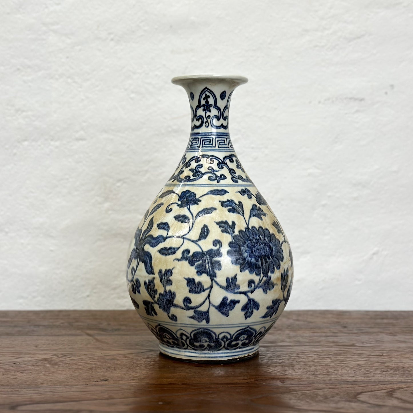 A globular porcelain vase with blue floral patterns on a white background, displayed against a neutral backdrop.