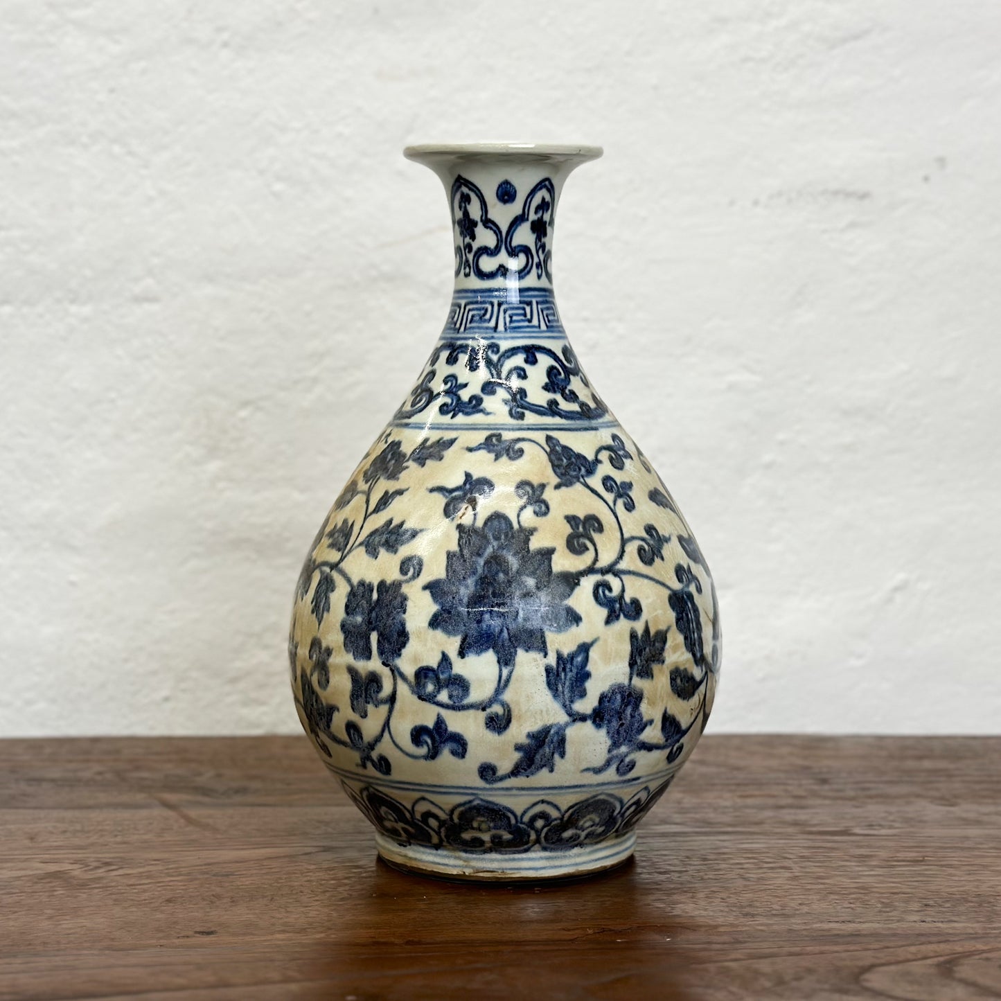 A globular porcelain vase with blue floral patterns on a white background, displayed against a neutral backdrop.