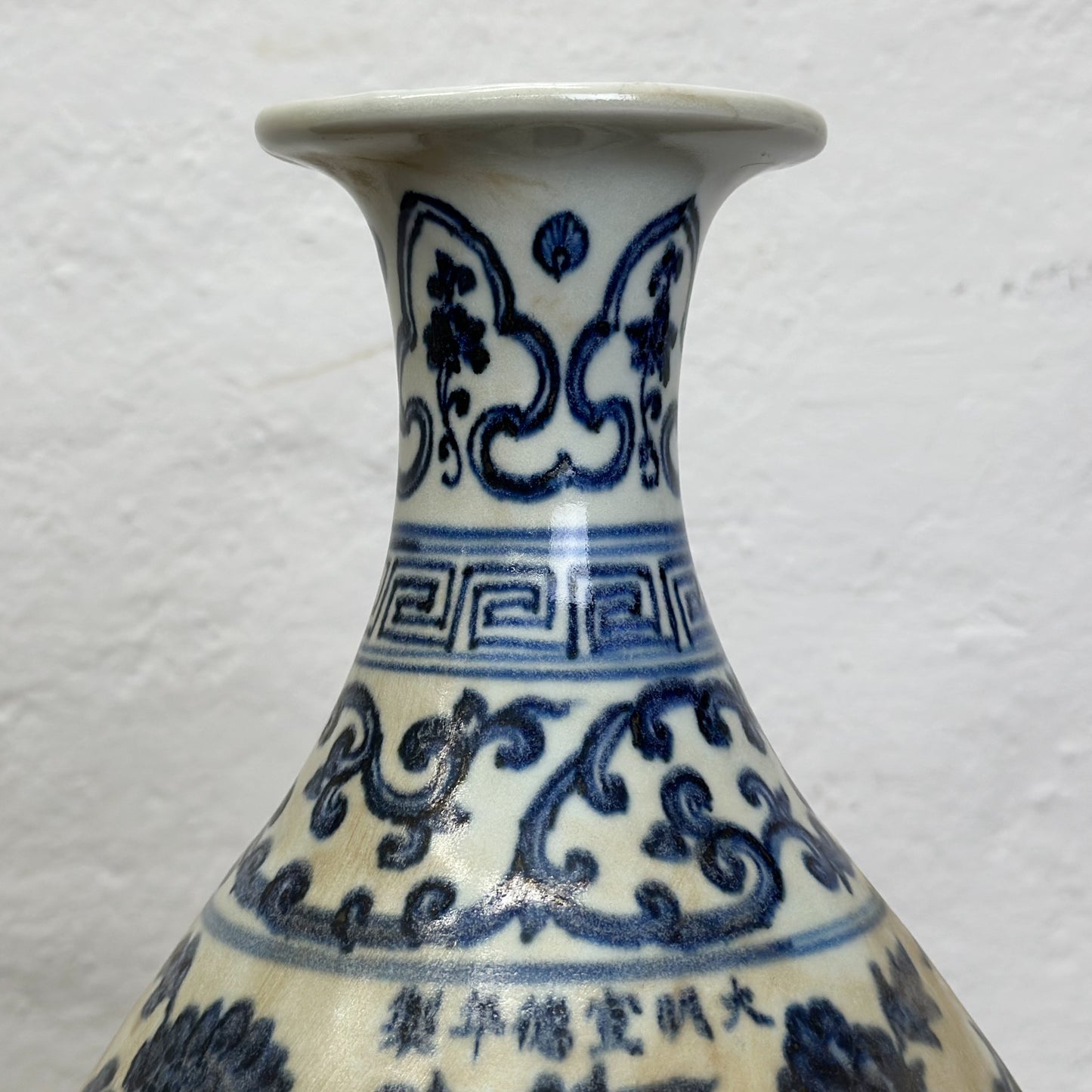 A globular porcelain vase with blue floral patterns on a white background, displayed against a neutral backdrop.