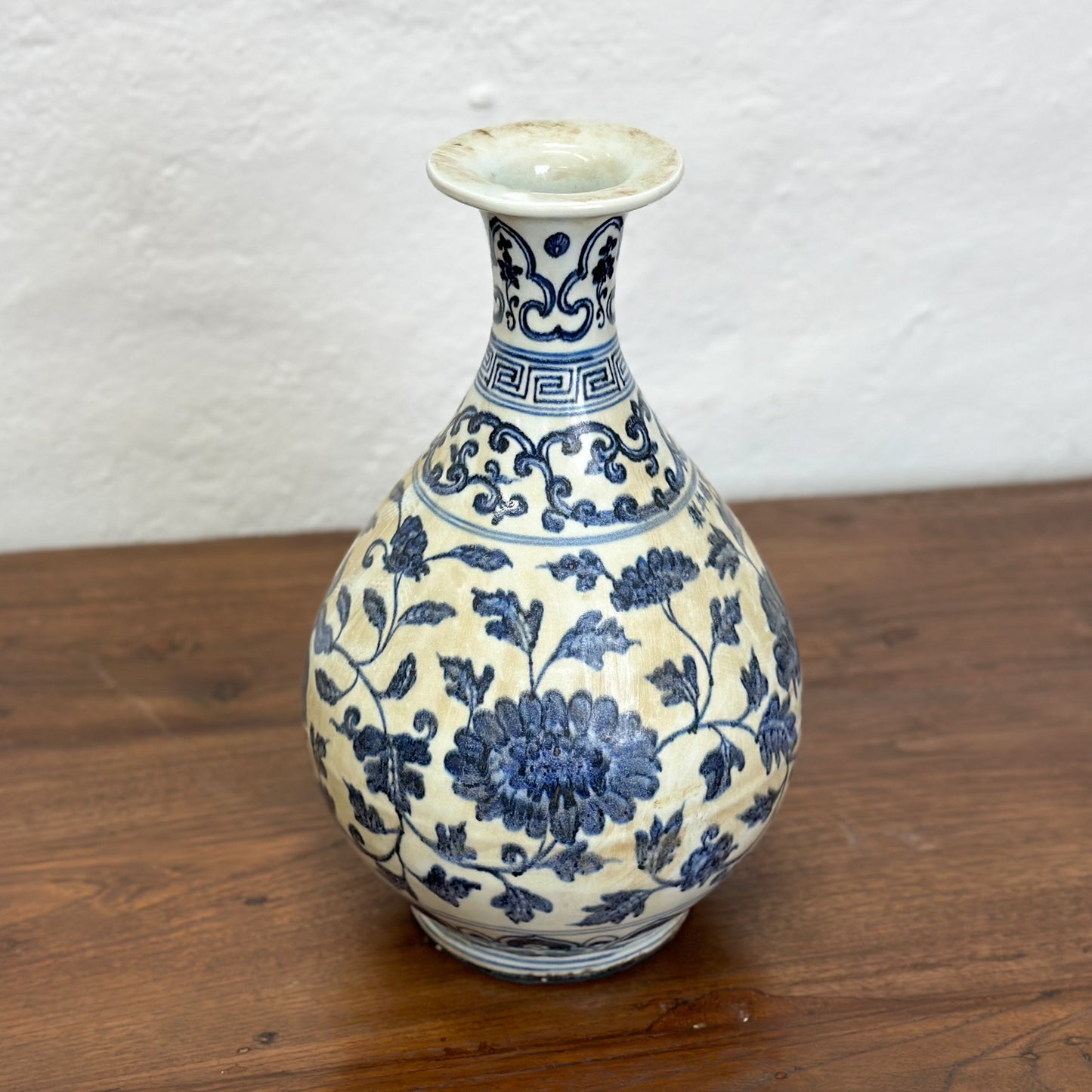 A globular porcelain vase with blue floral patterns on a white background, displayed against a neutral backdrop.
