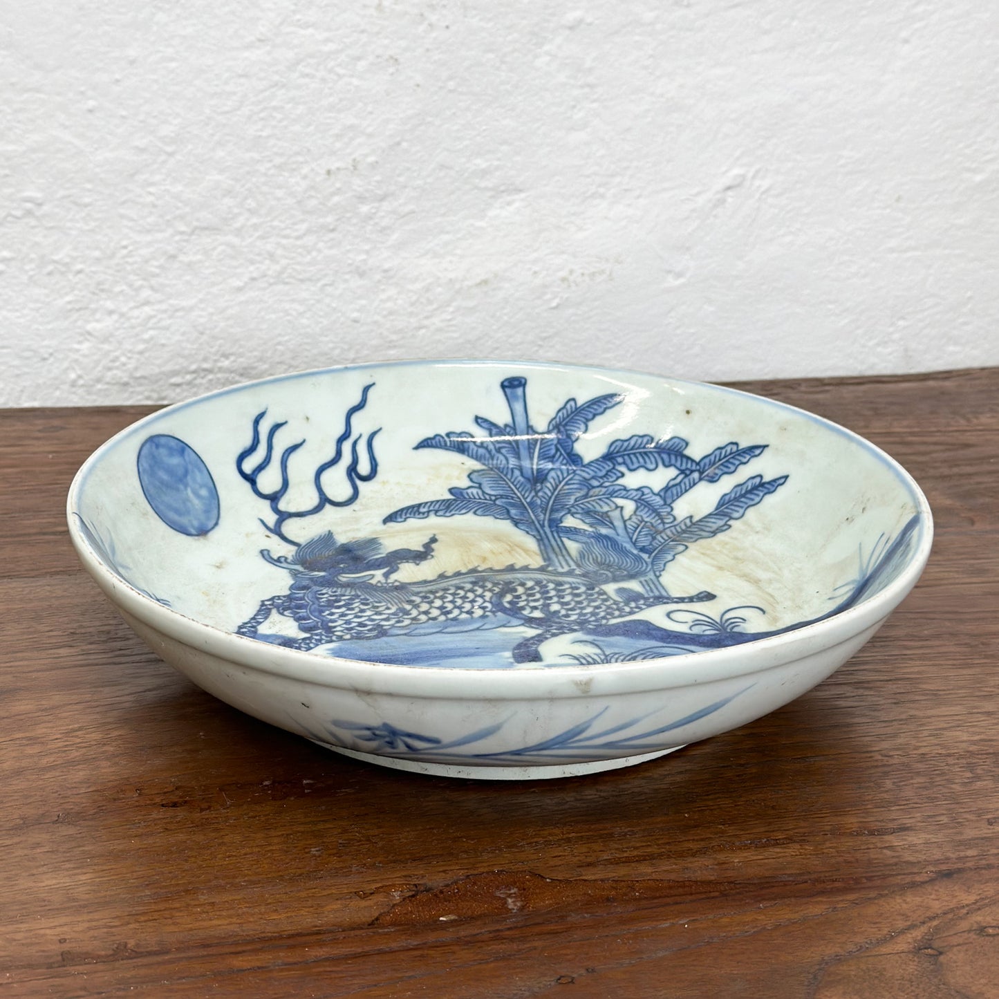 A porcelain plate with blue dragon illustration against a white background, displayed on a wooden surface.