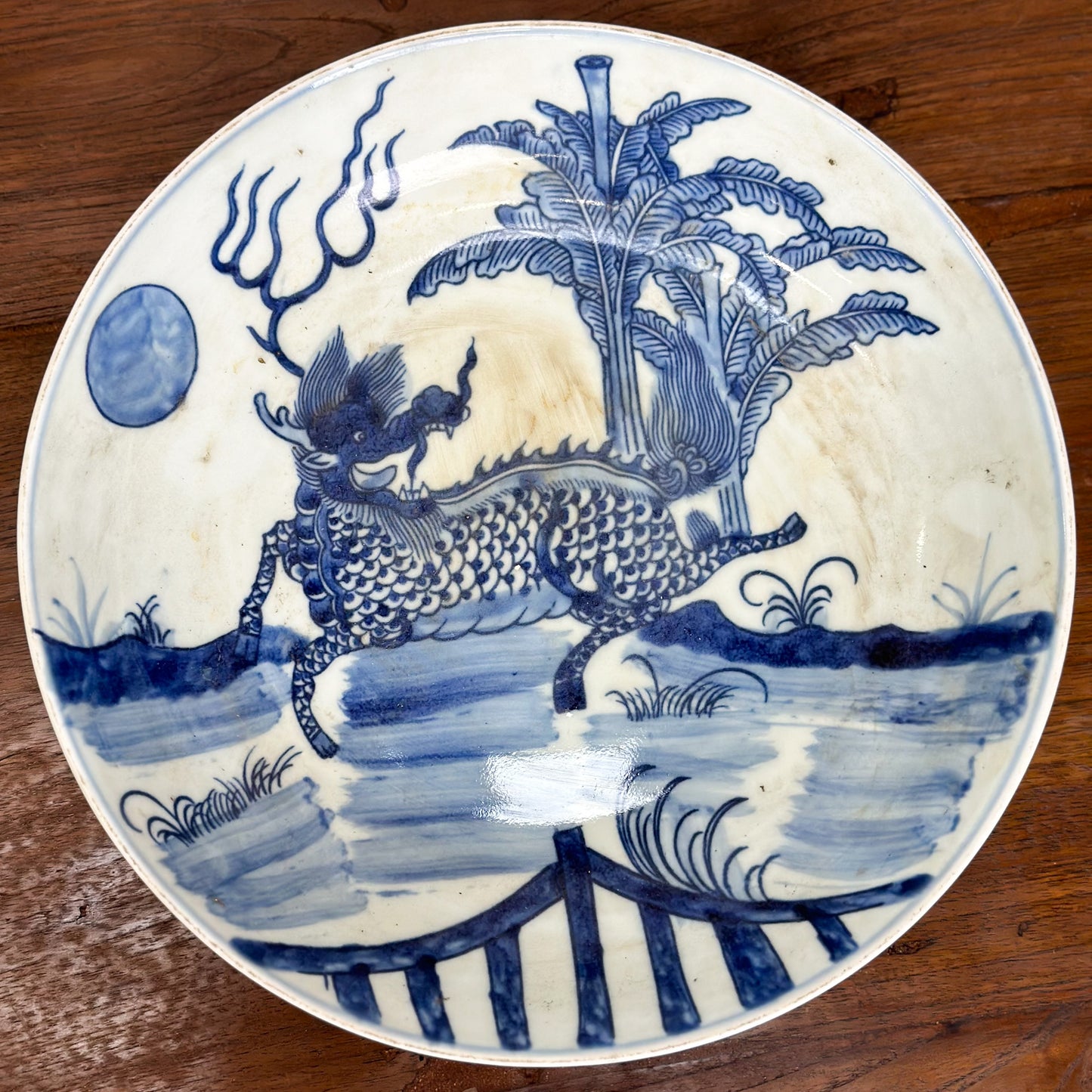 A porcelain plate with blue dragon illustration against a white background, displayed on a wooden surface.