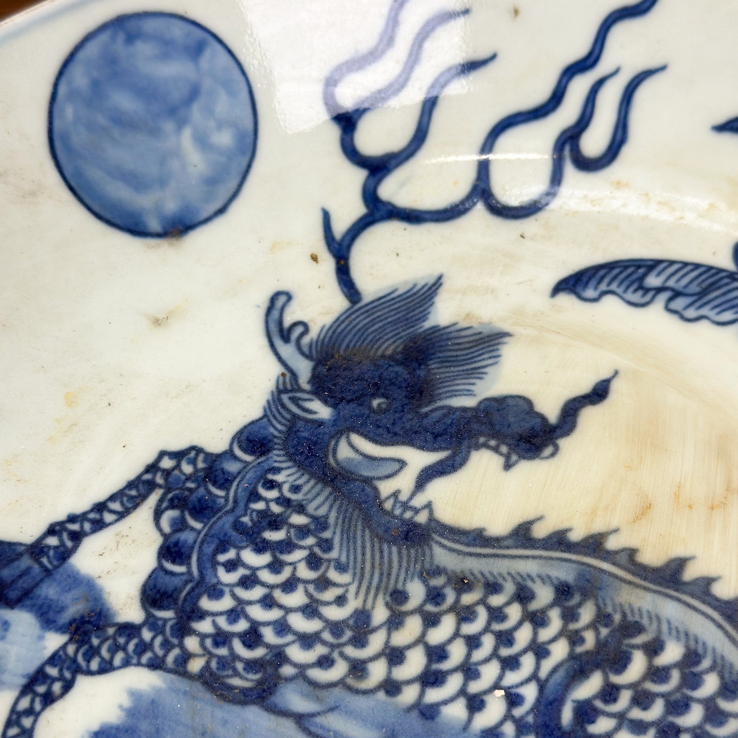 A porcelain plate with blue dragon illustration against a white background, displayed on a wooden surface.