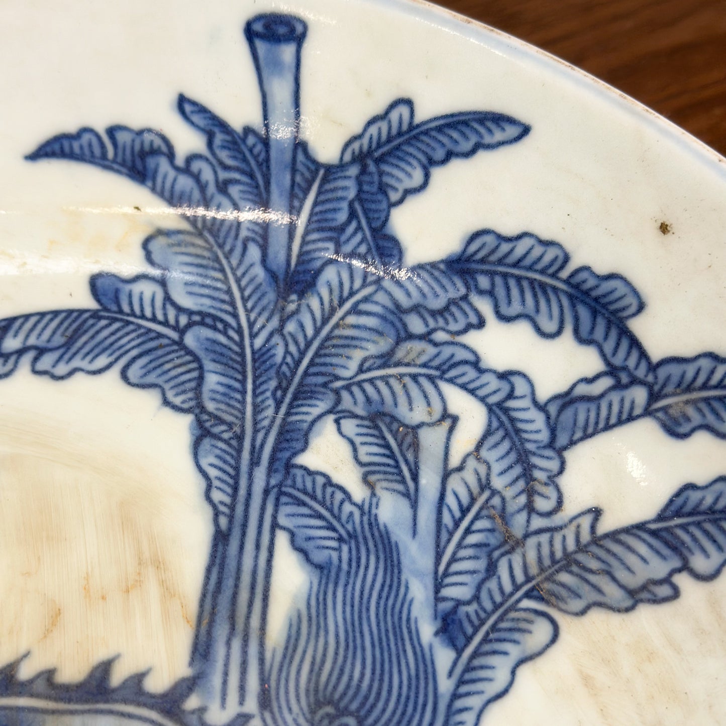 A porcelain plate with blue dragon illustration against a white background, displayed on a wooden surface.