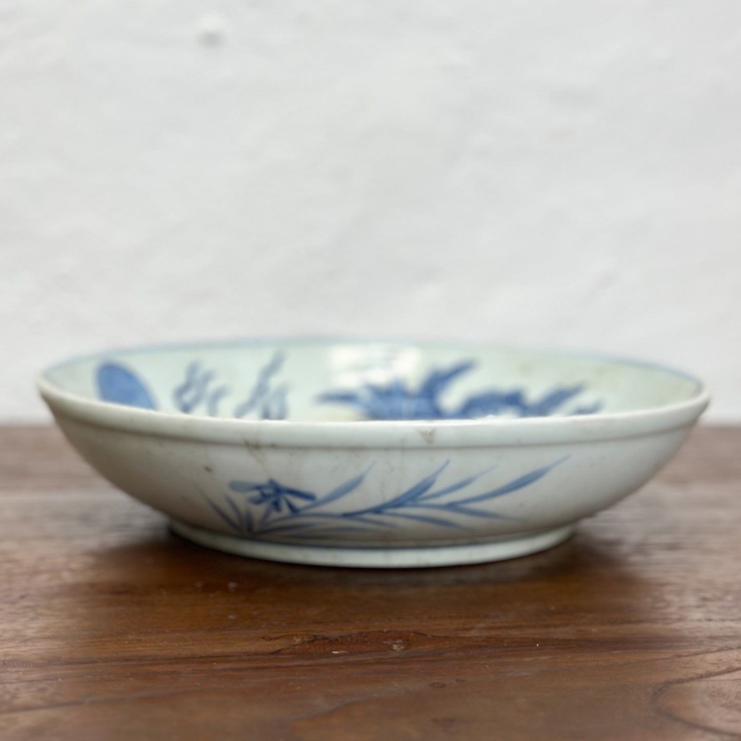 A porcelain plate with blue dragon illustration against a white background, displayed on a wooden surface.