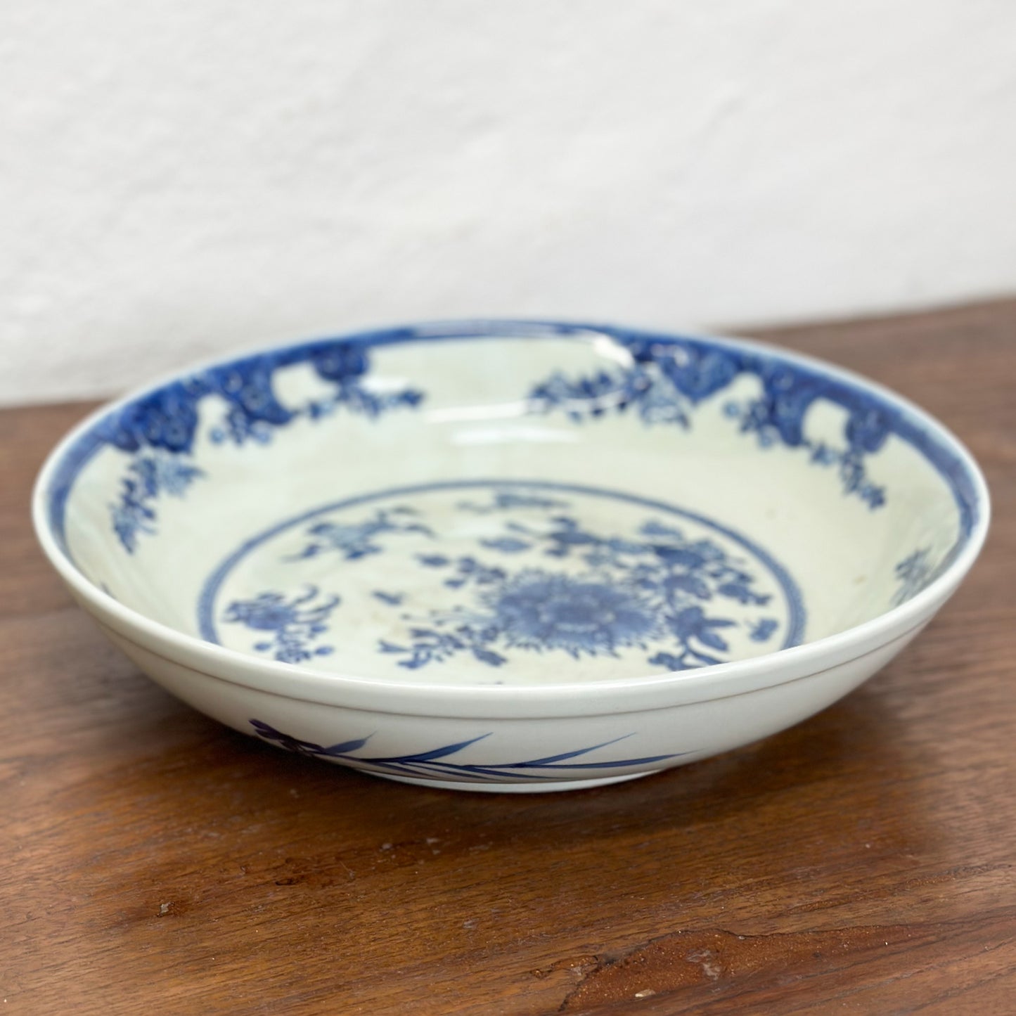A round porcelain plate with blue floral patterns on a white background, displayed on a wooden surface.
