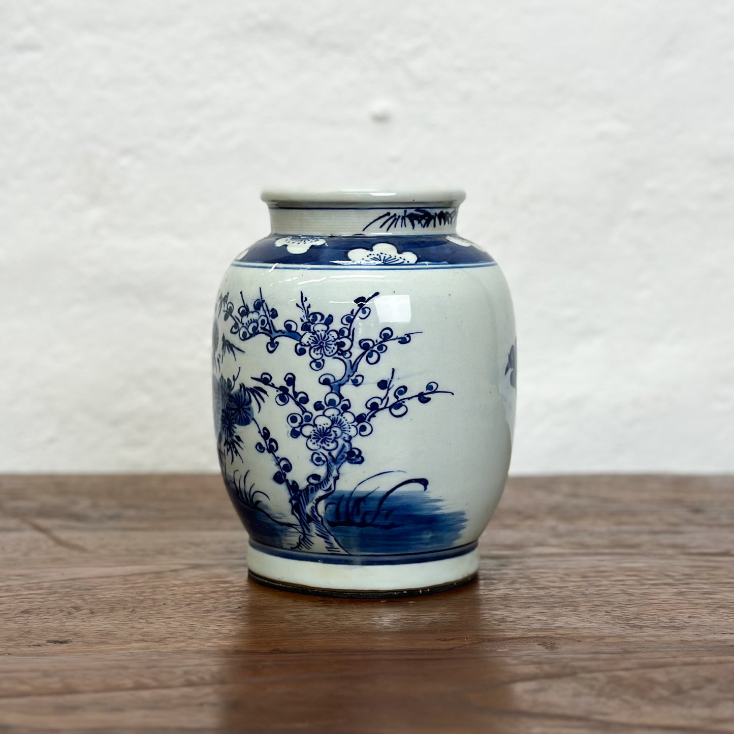 A blue and white porcelain vase with floral and tree patterns, displayed against a neutral background.