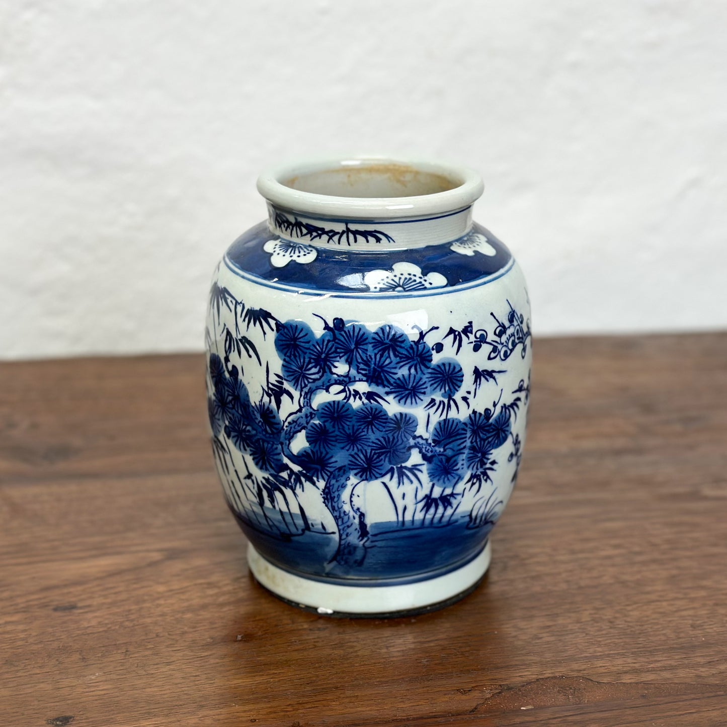 A blue and white porcelain vase with floral and tree patterns, displayed against a neutral background.